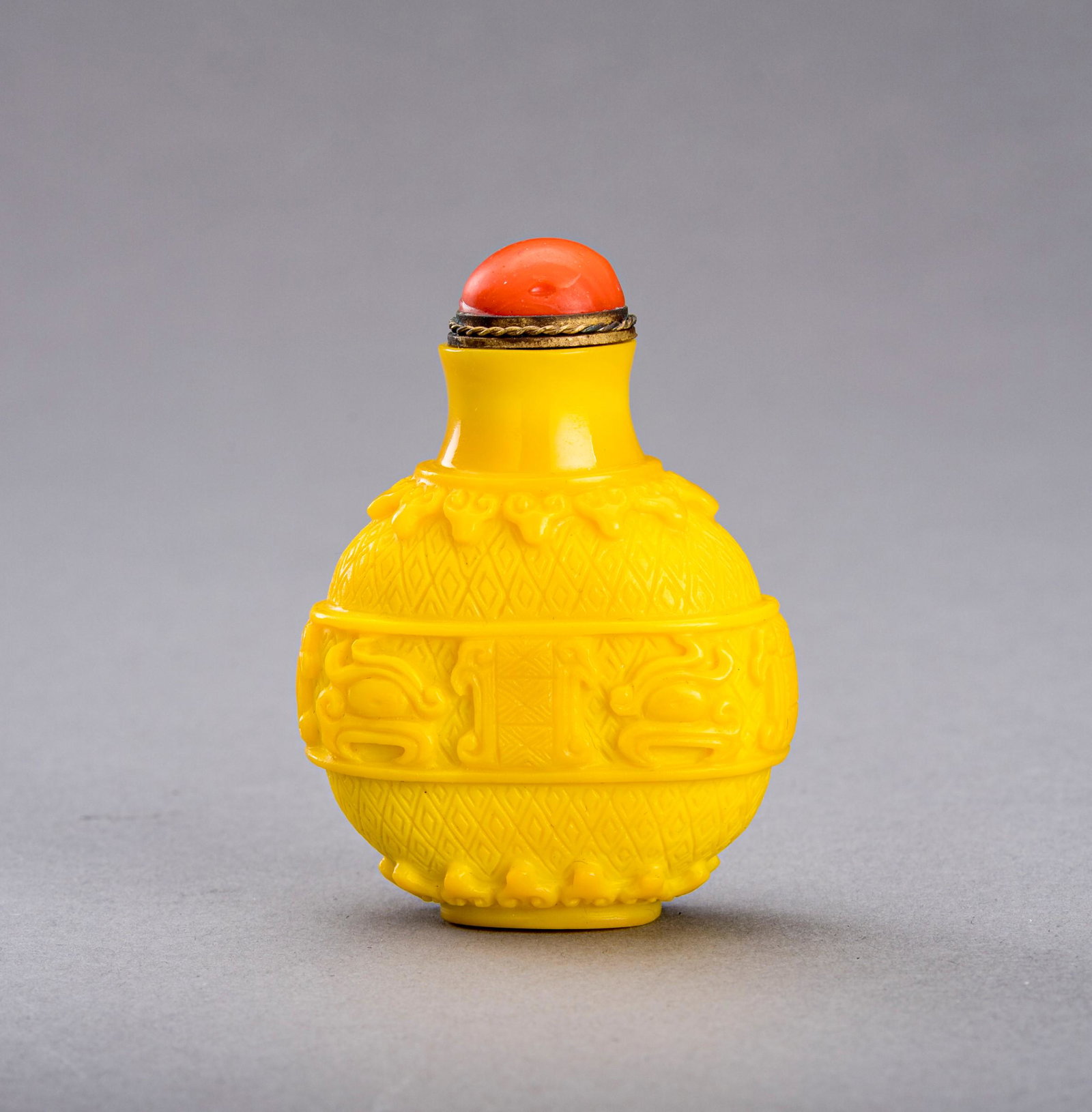 AN ARCHAISTIC YELLOW GLASS SNUFF BOTTLE, c. 1920s: AN ARCHAISTIC YELLOW GLASS SNUFF BOTTLE, c. 1920s China, late Qing Dynasty (1644-1912) - Republic period (1912-1949). Of compressed globular form, supported on an oval foot ring, carved with a band of