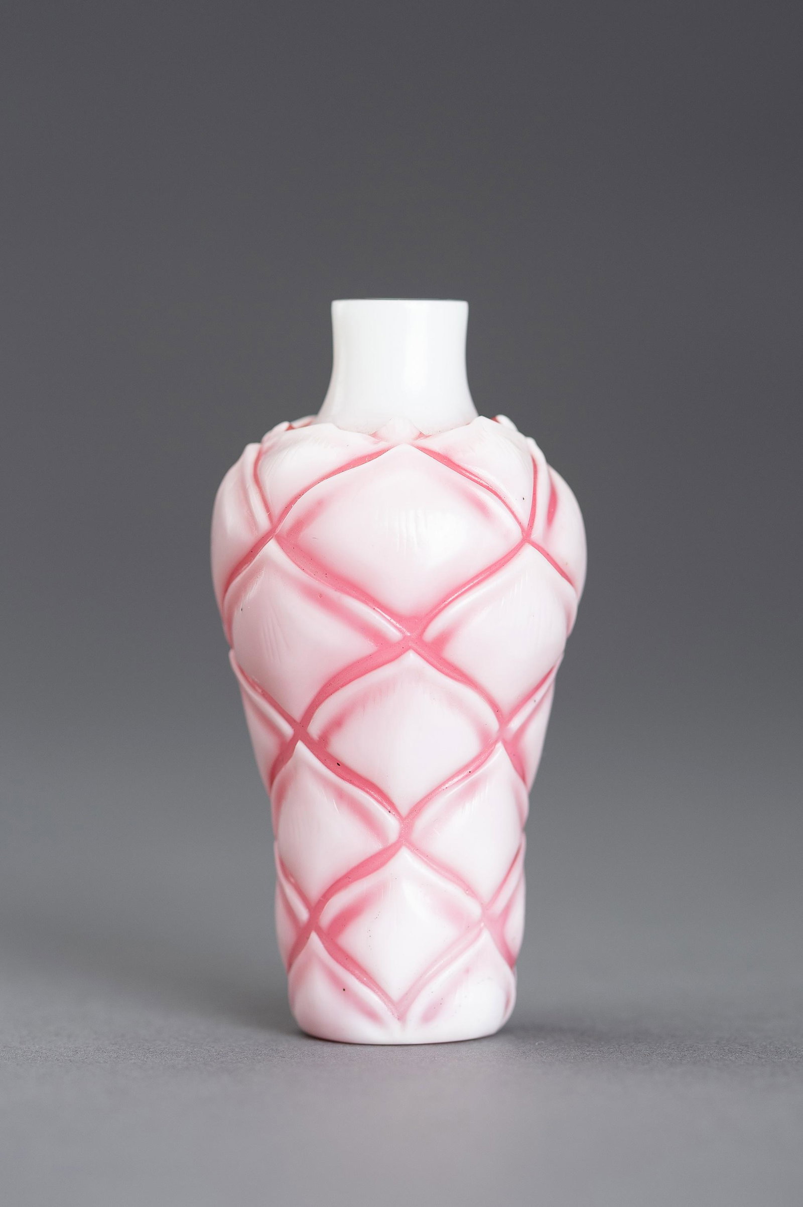 A SANDWICHED PINK GLASS 'LOTUS' SNUFF BOTTLE: A SANDWICHED PINK GLASS 'LOTUS' SNUFF BOTTLE China, Republic period (1912-1949). Of baluster form, rising from a circular foot to a straight neck, the body neatly carved and incised with seven rows of