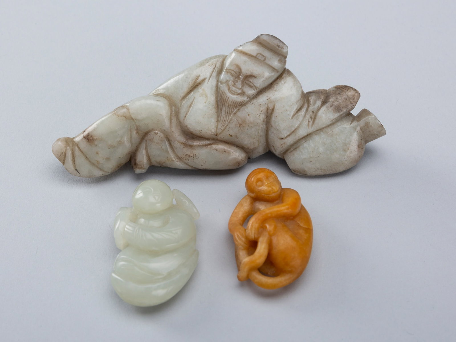 A GROUP OF THREE JADE PENDANTS AND FIGURES, 19TH CENTURY: A GROUP OF THREE JADE PENDANTS AND FIGURES, 19TH CENTURY China, late Qing Dynasty (1644-1912). One depicting the Chinese poet Li Bai, carved reclining, supporting himself in a wine jar, and wearing vo