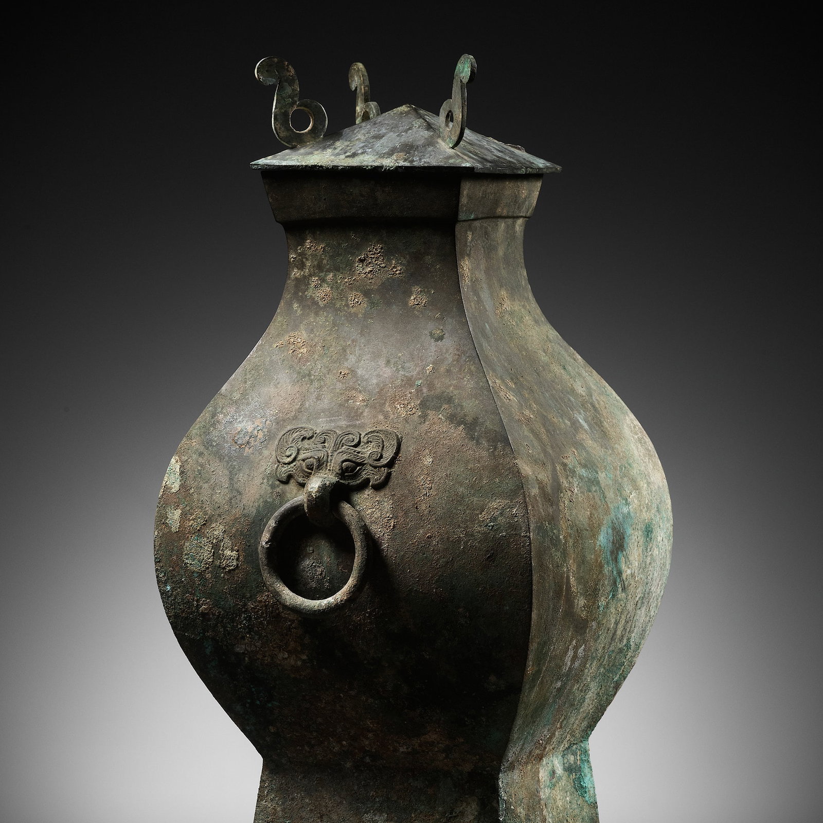 A LARGE BRONZE STORAGE VESSEL AND COVER, FANGHU, HAN DYNASTY: A LARGE BRONZE STORAGE VESSEL AND COVER, FANGHU, HAN DYNASTY China, 206 BC to AD 220. The faceted pear-shaped body raised on a slightly spreading square foot and applied to opposing sides with taotie 