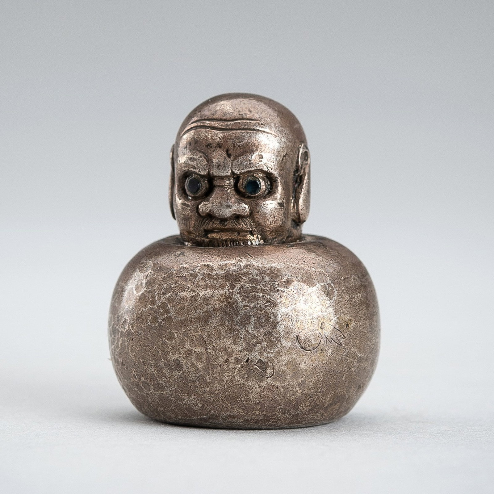 A RARE METAL SEAL OF DARUMA: A RARE METAL SEAL OF DARUMA 20th century The unusual seal of compressed globular form, depicting Daruma with a disgruntled expression, big eyes with inlaid pupils, and elongate earlobes. The seal face