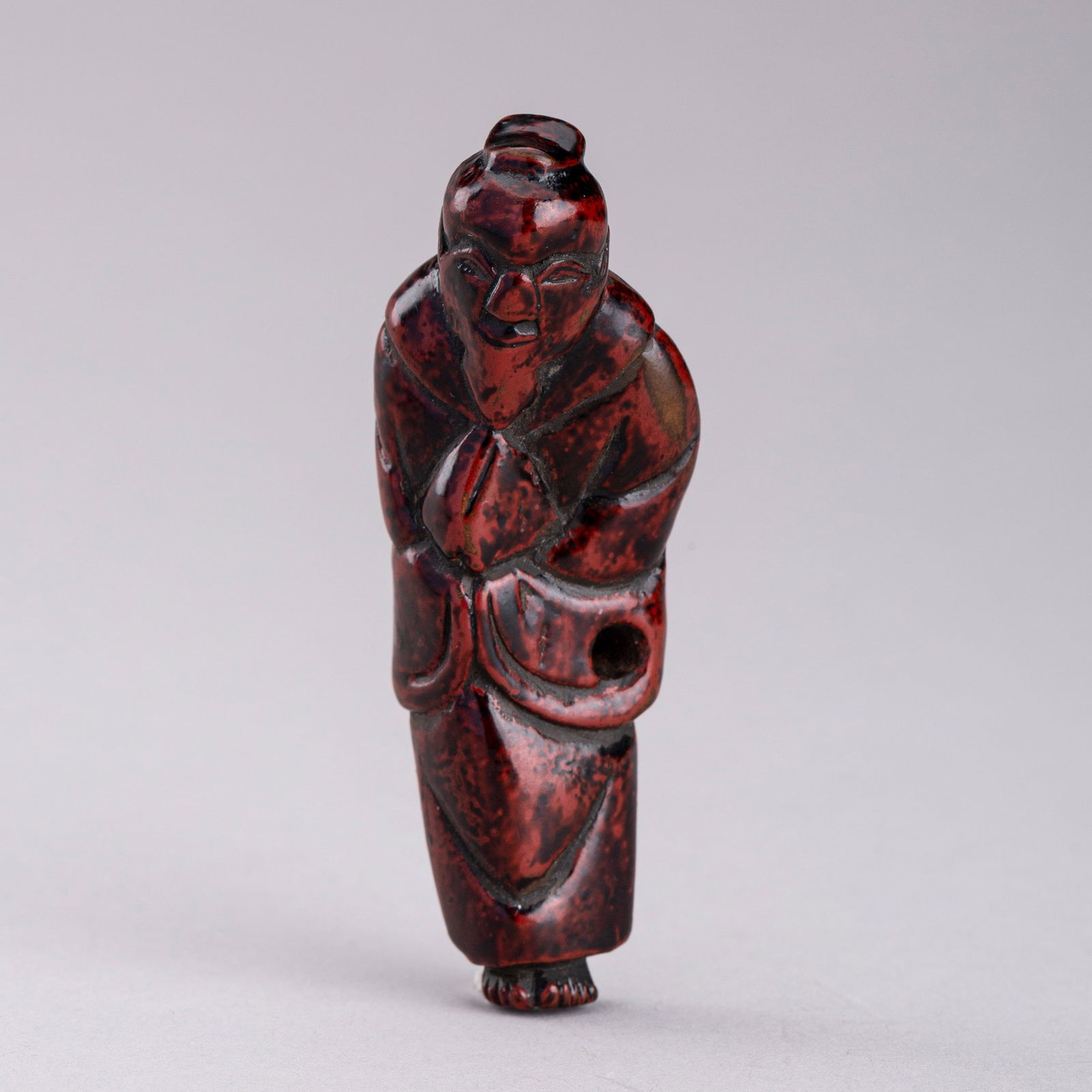 A LACQUERED WOOD NETSUKE OF A SAGE, EDO PERIOD: A LACQUERED WOOD NETSUKE OF A SAGE, EDO PERIOD Japan, early 19th century, Edo period (1615-1868)The wood netsuke lacquered in negoro-red and black, depicting a sage cloaked in a voluminous robe with l