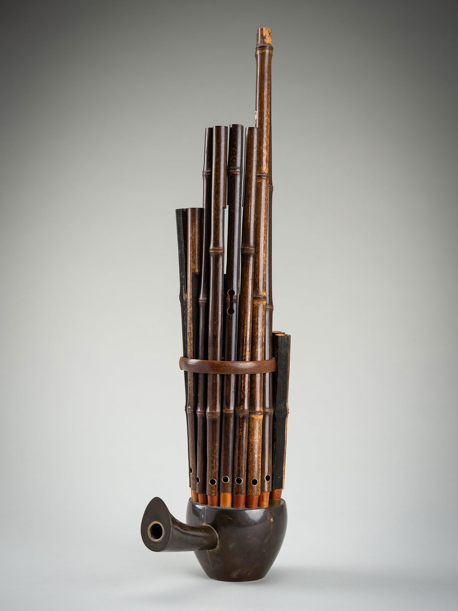 A BAMBOO SHENG (MOUTH ORGAN): A BAMBOO SHENG (MOUTH ORGAN) China, 20th century. The bamboo pipes set into a metal base with slanted mouthpiece and held together by bamboo fittings. One pipe with a sticker reading 'product of Beiji
