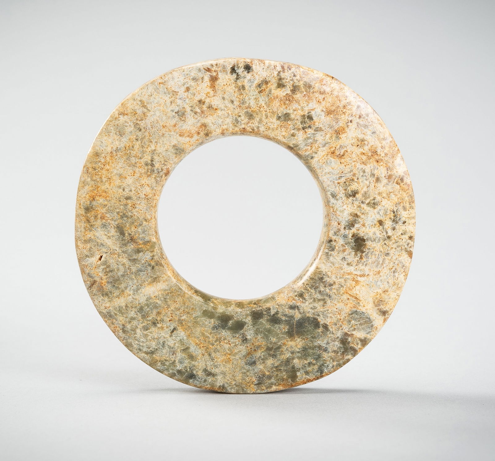 A JADE DISC, LIANGZHU CULTURE OR LATER: A JADE DISC, LIANGZHU CULTURE OR LATER China, possibly Liangzhu culture, c. 2600-2300 BC or later. Of irregular thickness, carved from a mottled celadon jade showing numerous creamy striations and pat