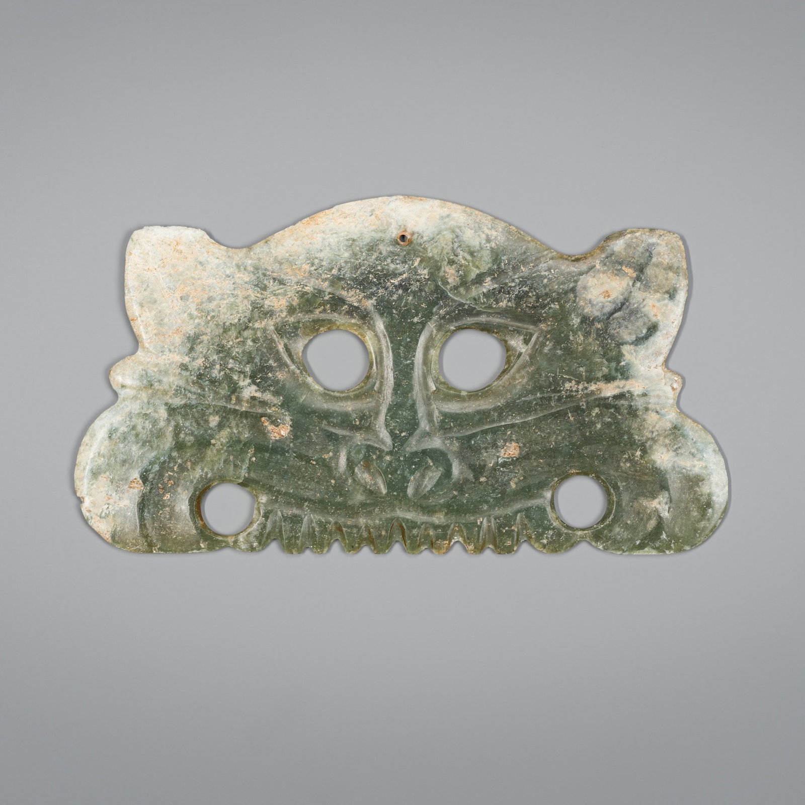 AN ARCHAISTIC HONGSHAN STYLE CELADON JADE TOOTHED ANIMAL MASK PENDANT: AN ARCHAISTIC HONGSHAN STYLE CELADON JADE TOOTHED ANIMAL MASK PENDANT China, late Qing Dynasty (1644-1912). Carved and pierced in the form of an animal mask, with circular eyes, wide snout, and horns.