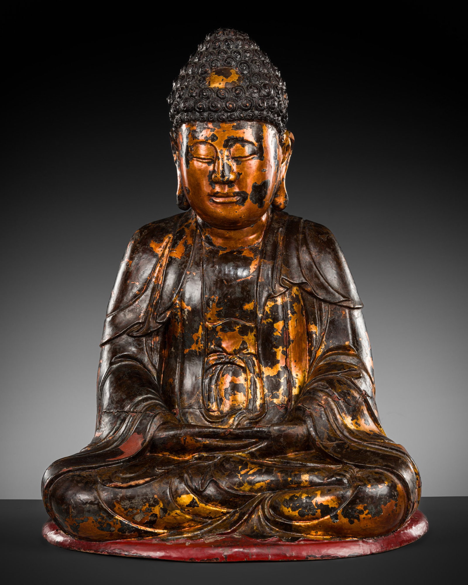 A MASSIVE GILT-LACQUERED WOOD FIGURE OF BUDDHA, VIETNAM, 17TH-18TH CENTURY: A MASSIVE GILT-LACQUERED WOOD FIGURE OF BUDDHA, VIETNAM, 17TH-18TH CENTURY Seated in dhyanasana on a red lacquered plinth, the hands lowered in dhyanamudra, wearing loose voluminous robes opening at t