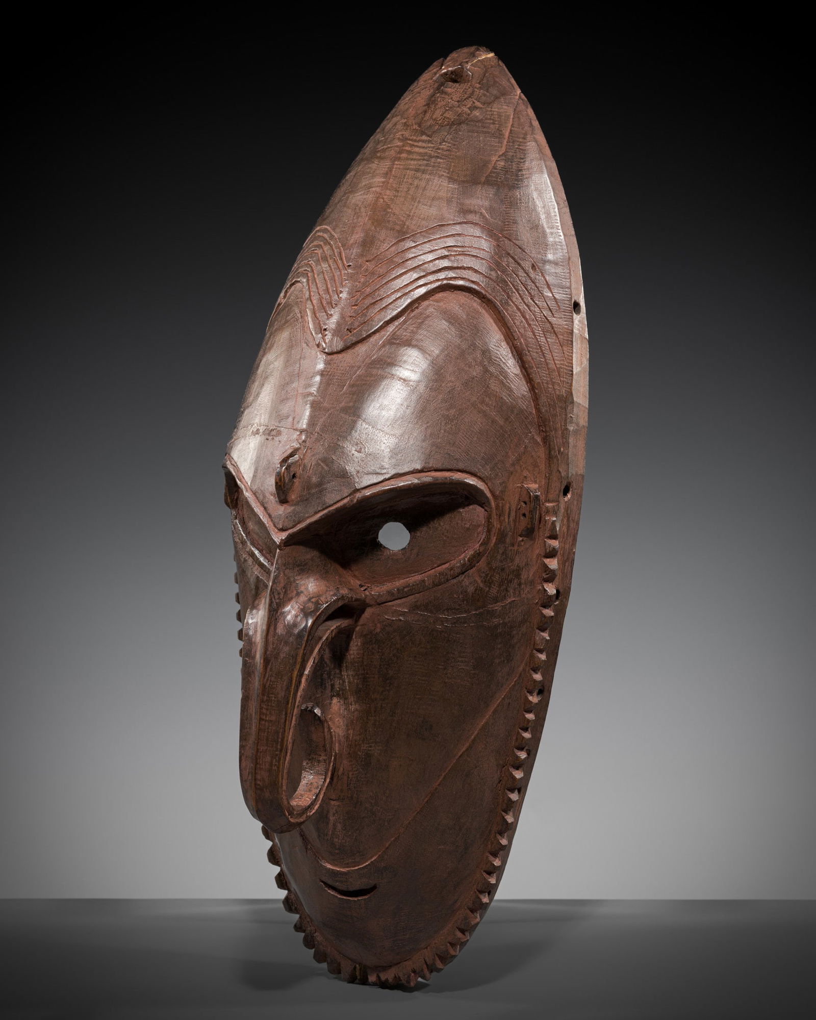 A CARVED WOOD MANGAN MASK OF A SPIRIT, BRAG, LOWER SEPIK RIVER: A CARVED WOOD MANGAN MASK OF A SPIRIT, BRAG, LOWER SEPIK RIVER Papua New Guinea, East Sepik Province. The oval face carved with a serrated beard, the nose and eye orbital area outlined with a shallow