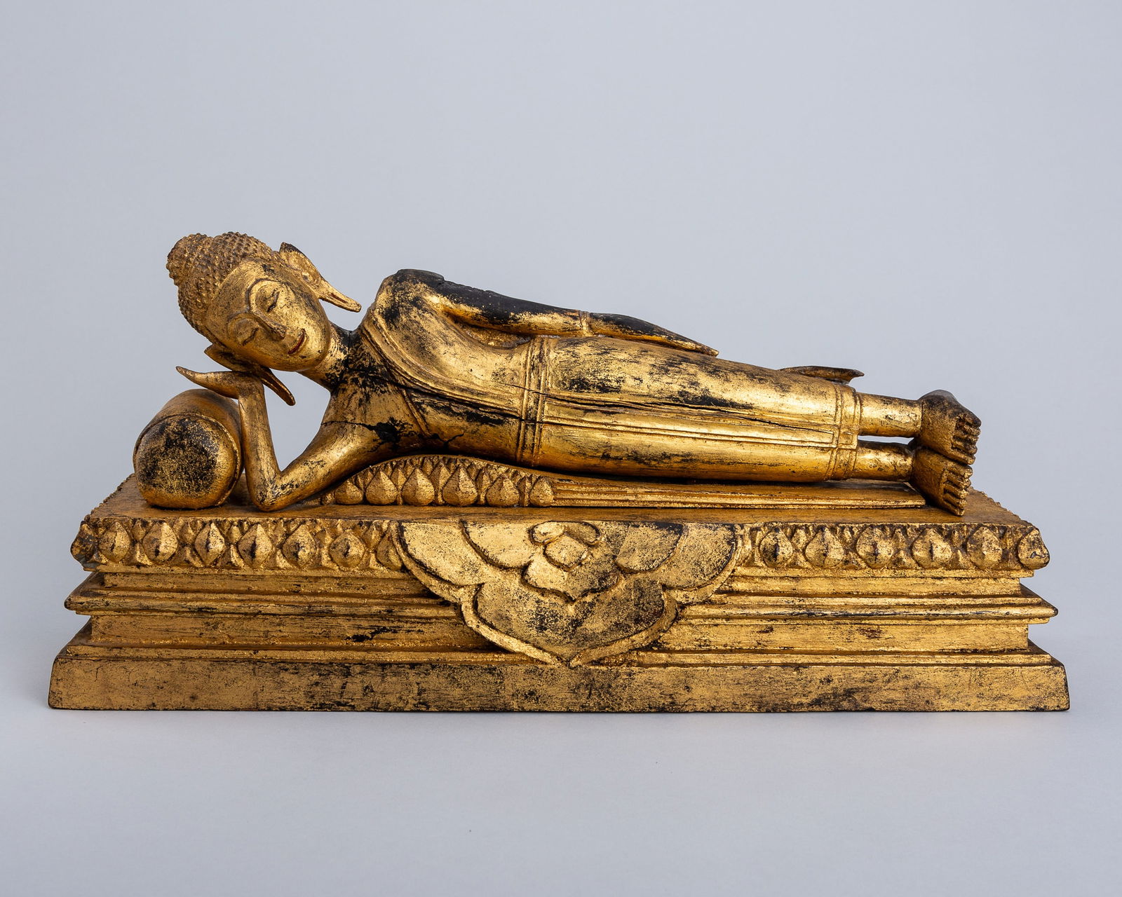 A GILT-LACQUERED WOOD FIGURE OF BUDDHA IN PARINIRVANA, LATE RATTANAKOSIN KINGDOM: A GILT-LACQUERED WOOD FIGURE OF BUDDHA IN PARINIRVANA, LATE RATTANAKOSIN KINGDOM Thailand, late Rattanakosin period (1782-1932). Carved reclining on a stepped base, the head held resting in one hand,