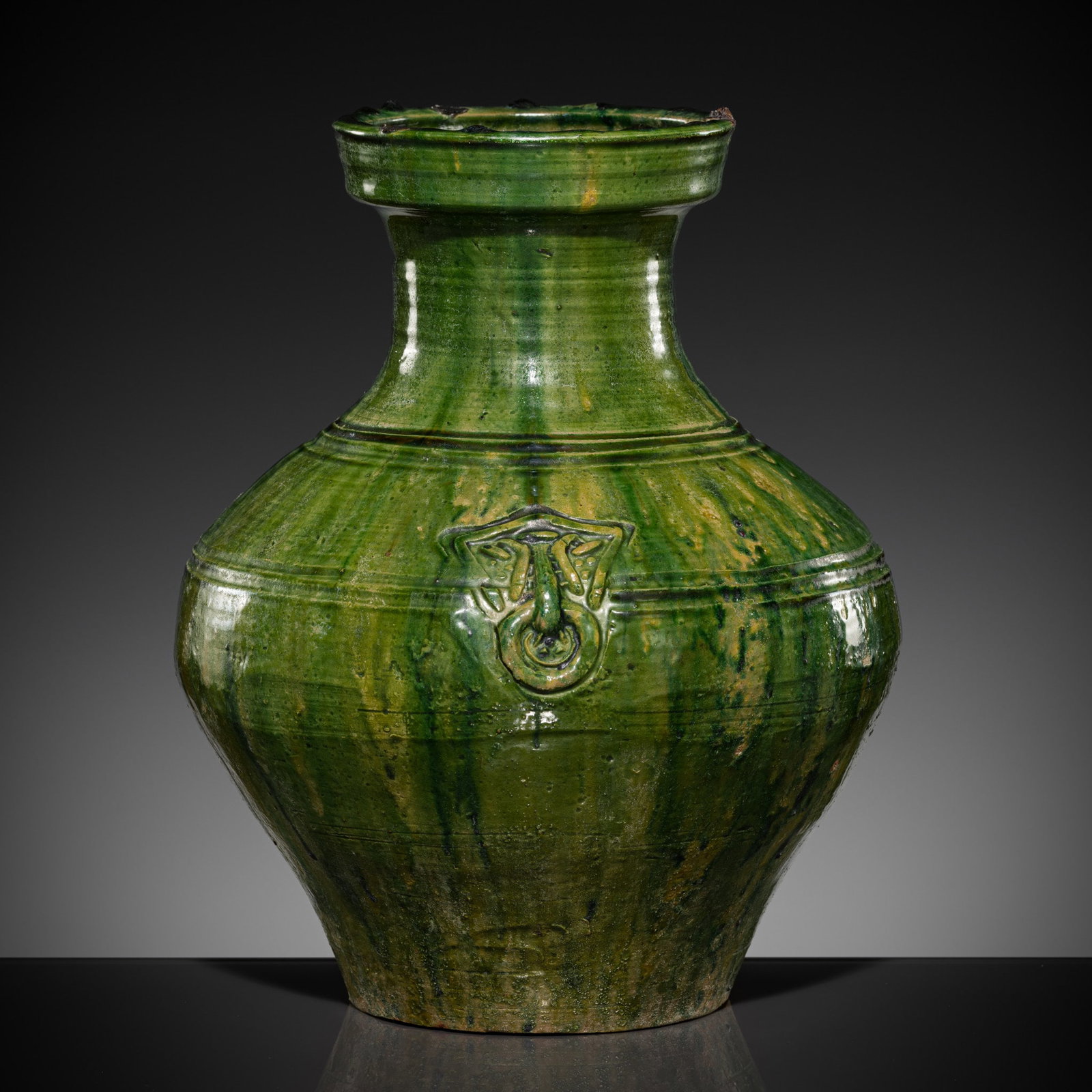 A GREEN-GLAZED POTTERY VASE, HU, HAN DYNASTY: A GREEN-GLAZED POTTERY VASE, HU, HAN DYNASTY China, 206 BC-220 AD. The robust pear-shaped body neatly incised with a double bow-string band overlaid on two sides by a pair of mask and mock-ring handle