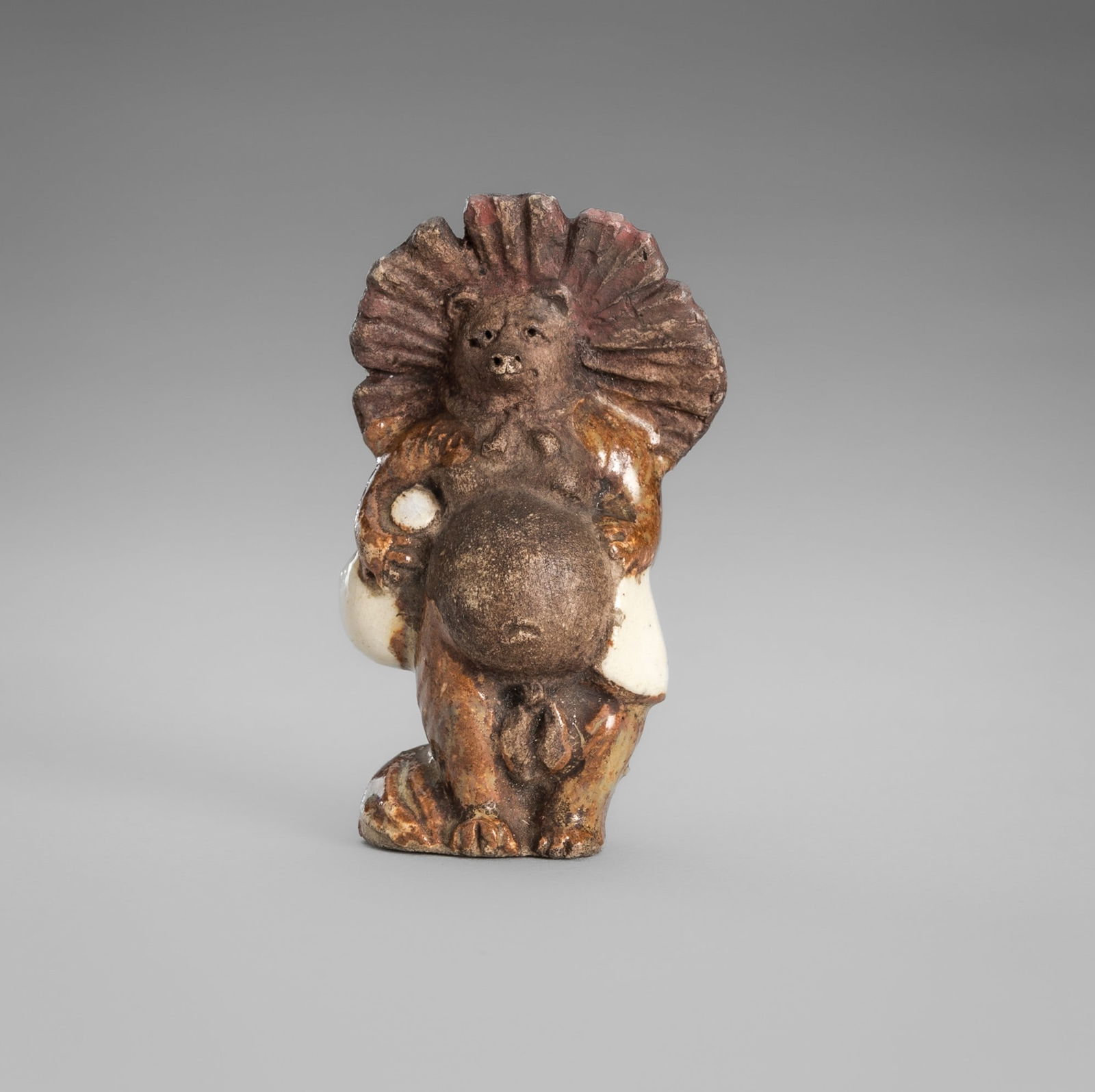 WAHEI: AN AMUSING CERAMIC NETSUKE OF A TANUKI DISGUISED AS A SAKE VENDOR: WAHEI: AN AMUSING CERAMIC NETSUKE OF A TANUKI DISGUISED AS A SAKE VENDOR By Wahei workshop, sealed Wahei 和平Japan, late 19th centuryFinely modelled standing, holding a sake flask in one