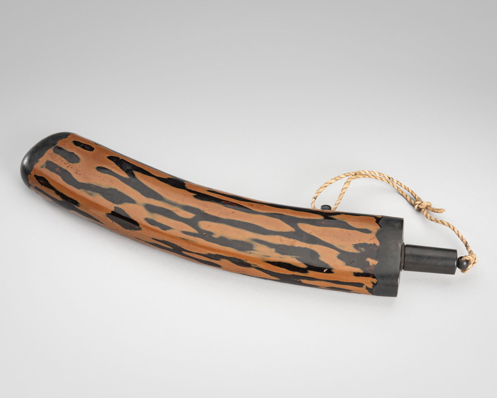 A RARE BROWN AND BLACK LACQUER KAYAKU-IRE (GUNPOWDER FLASK): A RARE BROWN AND BLACK LACQUER KAYAKU-IRE (GUNPOWDER FLASK) UnsignedJapan, late 19th centuryThe black and brown lacquered kayaku-ire (gunpowder flask), of flattened, curved tubular form, the surface