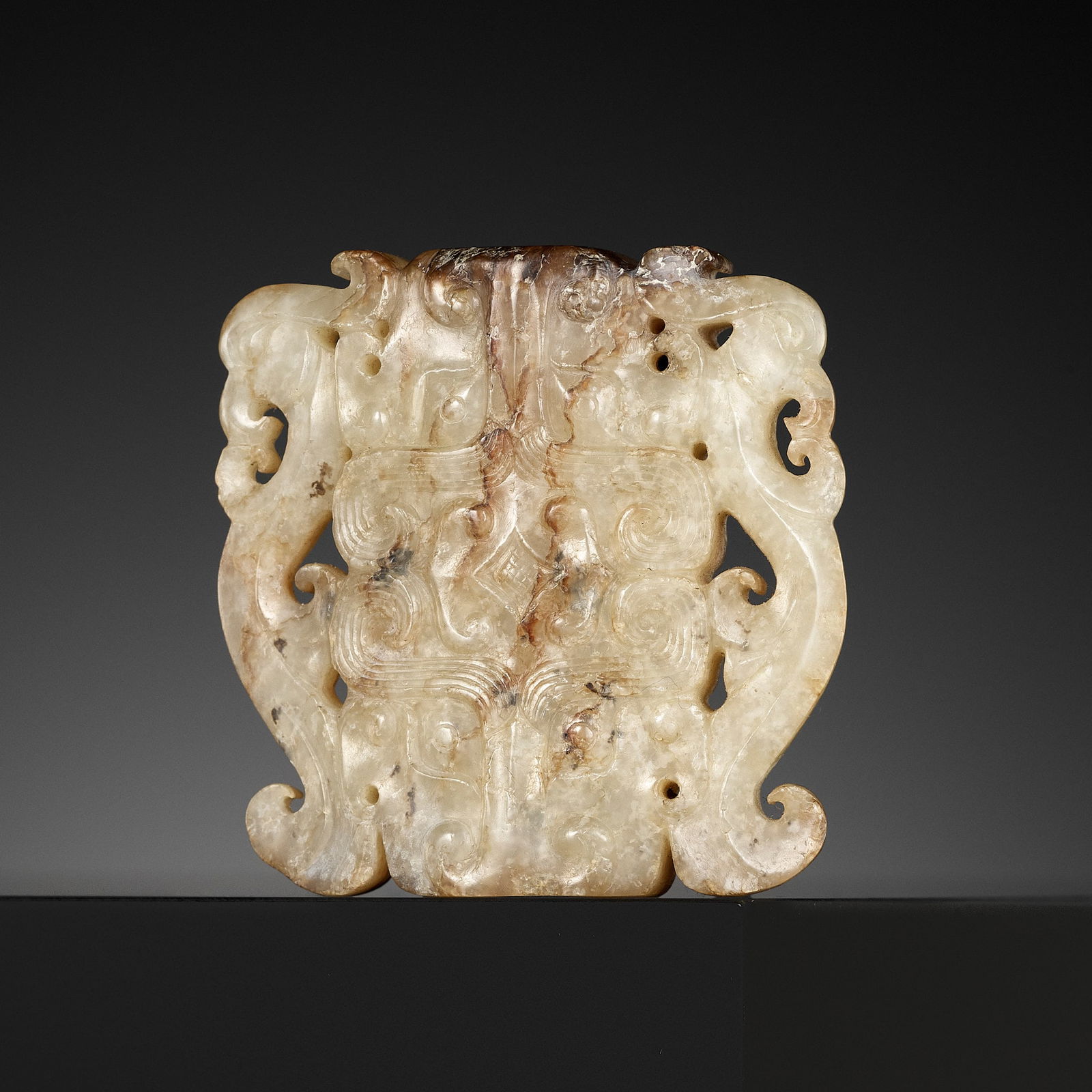 A WHITE AND RUSSET JADE 'BEAST MASK AND PHOENIX' PENDANT, ZHOU DYNASTY: A WHITE AND RUSSET JADE 'BEAST MASK AND PHOENIX' PENDANT, ZHOU DYNASTY China, 1046 BC to 256 BC. Carved on each side, the ornament with a central rectangular section incised with a pair of confronting
