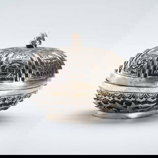A LIDDED SILVER MINIATURE BOX: A LIDDED SILVER MINIATURE BOX South China / Vietnam, 1880s &#8211; 1920s. Of round form, raised on a short circular base, finely embossed, the box encircled by leafy tendrils and floral decor. The dom