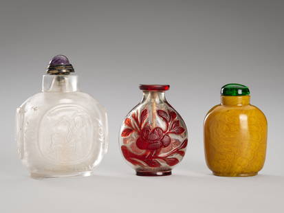 A GROUP OF THREE GLASS AND ROCK CRYSTAL SNUFF BOTTLES, QING DYNASTY: A GROUP OF THREE GLASS AND ROCK CRYSTAL SNUFF BOTTLES, QING DYNASTY China, Qing Dynasty (1644-1912). The first a large rock crystal bottle of rounded square form, carved with roundels, one enclosing S