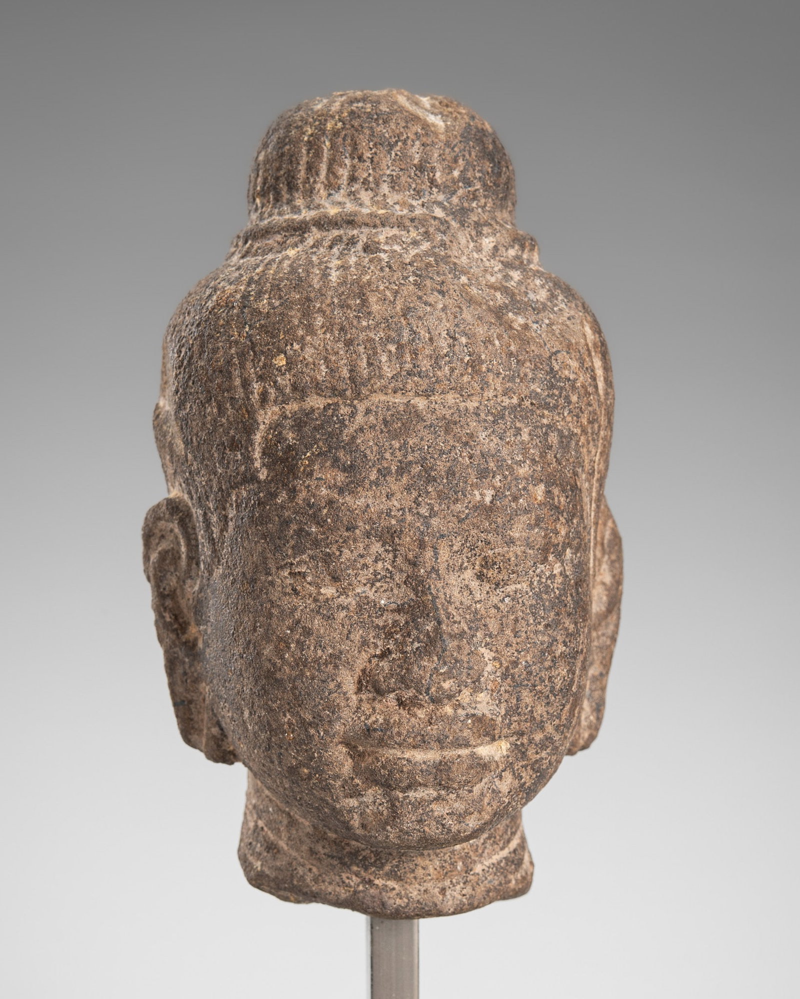 A SMALL SANDSTONE HEAD OF A MALE DEITY, ANGKOR PERIOD: A SMALL SANDSTONE HEAD OF A MALE DEITY, ANGKOR PERIOD Khmer Empire, 12th-13th century. Finely carved with a serene expression, the oval face shows thick lips, a broad nose and almond shaped eyes, all