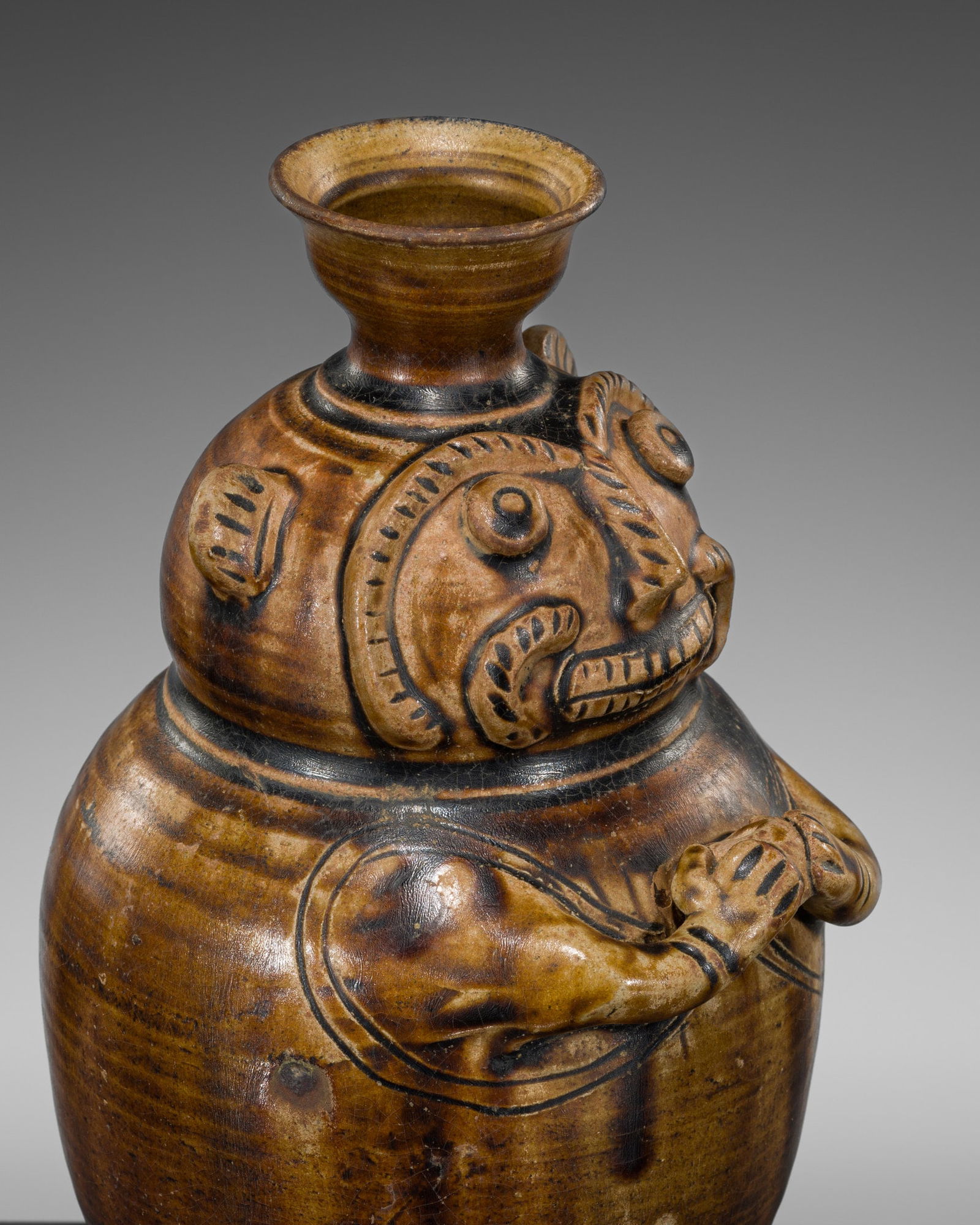 A BROWN-GLAZED STONEWARE JAR IN THE FORM OF A BEARDED MAN: A BROWN-GLAZED STONEWARE JAR IN THE FORM OF A BEARDED MAN Thailand, 19th to early 20th century. The anthropomorphic gourd-shaped body is supported on a flared foot and rising to a cup-shaped mouth. Th
