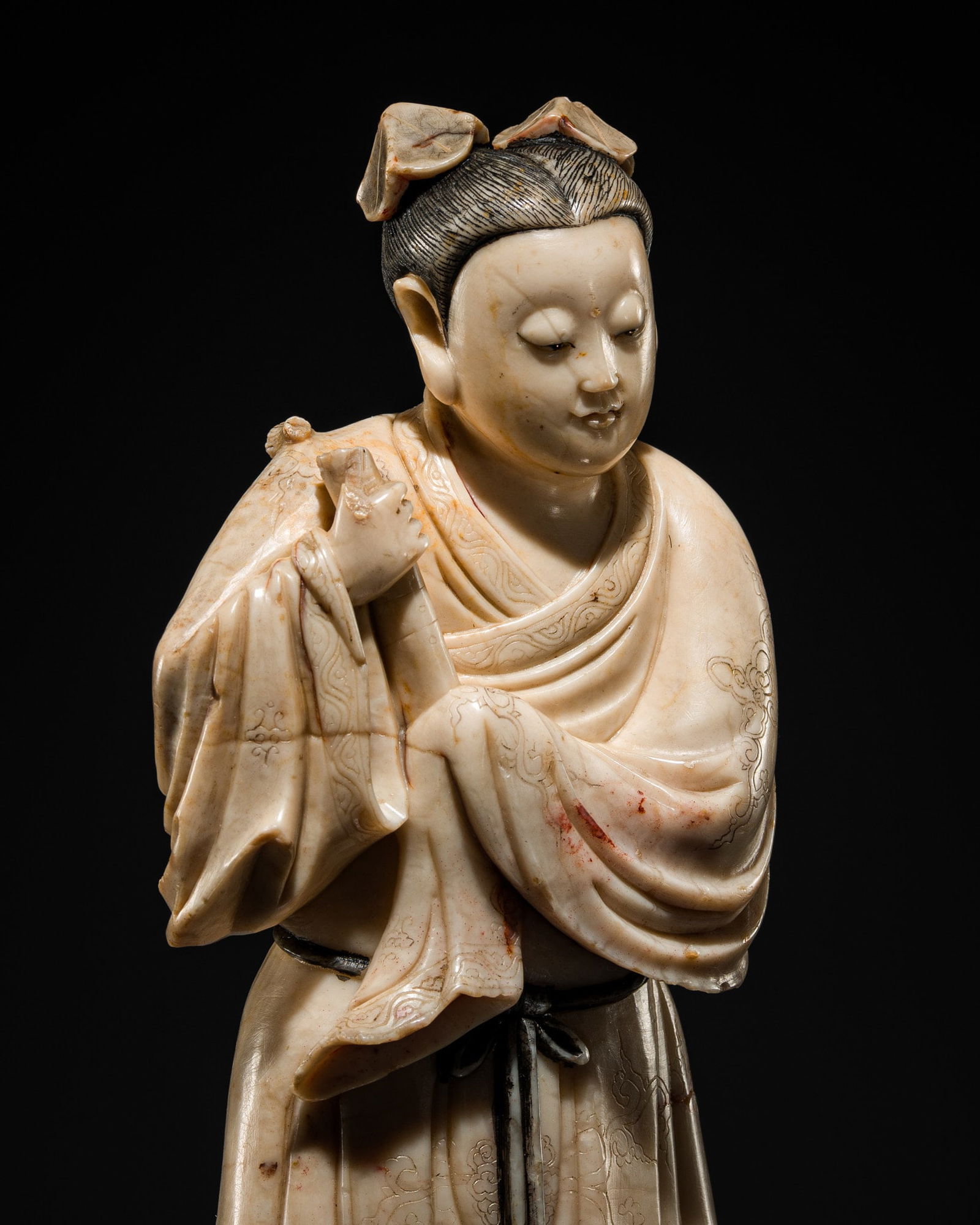 A SOAPSTONE 'GAOSHAN' FIGURE OF HAN XIANGZI, EARLY QING DYNASTY: A SOAPSTONE 'GAOSHAN' FIGURE OF HAN XIANGZI, EARLY QING DYNASTY China, 17th-18th century. Naturalistically carved in the form of the Immortal depicted standing, holding a flute with both hands, adorne