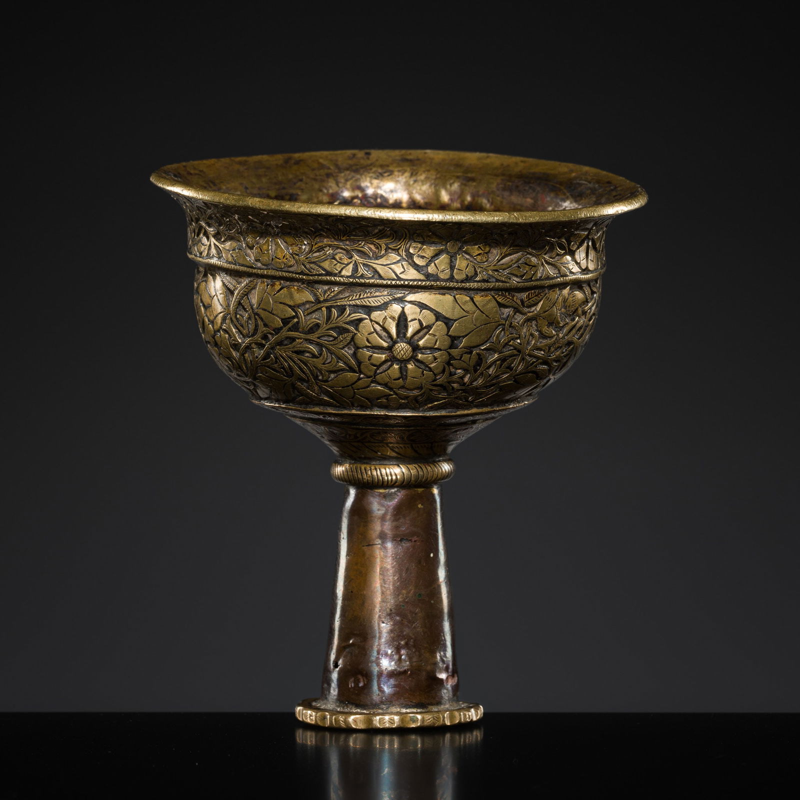 A BRONZE AND COPPER HOOKAH BOWL, 19TH CENTURY: A BRONZE AND COPPER HOOKAH BOWL, 19TH CENTURY India, Ladakh. The bronze bowl of upturned goblet form, pierced to its center and delicately decorated with bands of floral vines issuing leaves, with a s