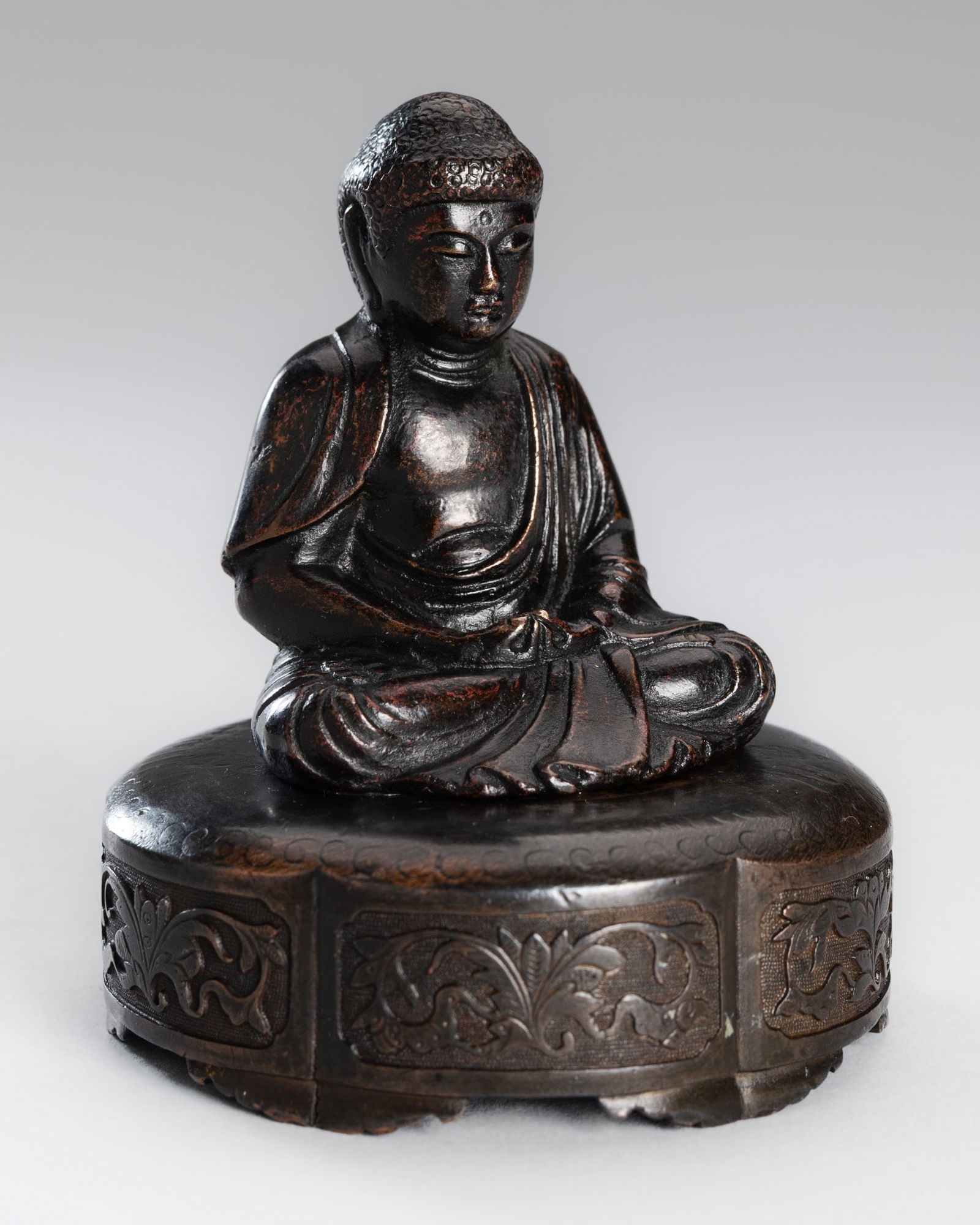 A SMALL COPPER ALLOY FIGURE OF BUDDHA: A SMALL COPPER ALLOY FIGURE OF BUDDHA Japan, Meiji period (1868-1912)Seated in dhyanasana atop a pedestal decorated to the sides with lobed panels enclosing foliate scrolls, the hands lowered in m