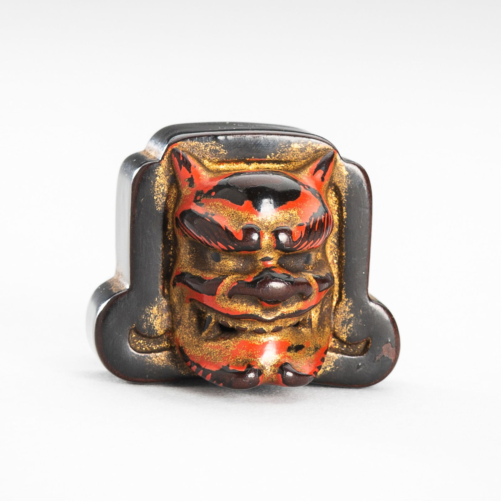 A SIGNED NEGORO LACQUER NETSUKE DEPICTING A ROOF TILE WITH ONI MASK: A SIGNED NEGORO LACQUER NETSUKE DEPICTING A ROOF TILE WITH ONI MASK SignedJapan, late 19th century, Edo period (1615-1868)The tile is carved on the front with an oni mask bearing a fierce expression