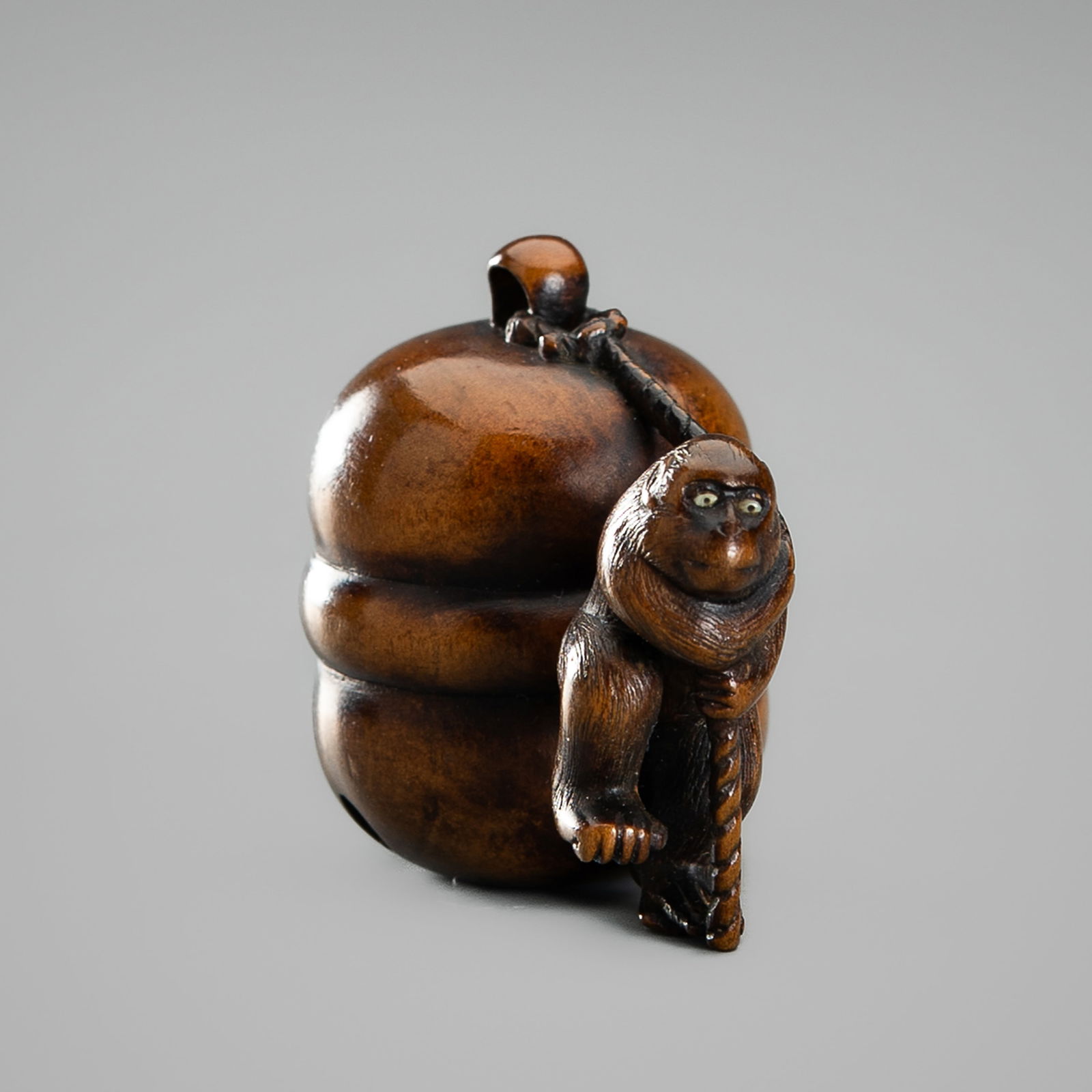 A WOOD NETSUKE OF A MONKEY PULLING A MOKUGYO BELL: A WOOD NETSUKE OF A MONKEY PULLING A MOKUGYO BELL Unsigned Japan, 18th century, Edo period (1615-1868)Finely carved as a little monkey pulling a large moguygo bell with a rope behind him, one leg rais