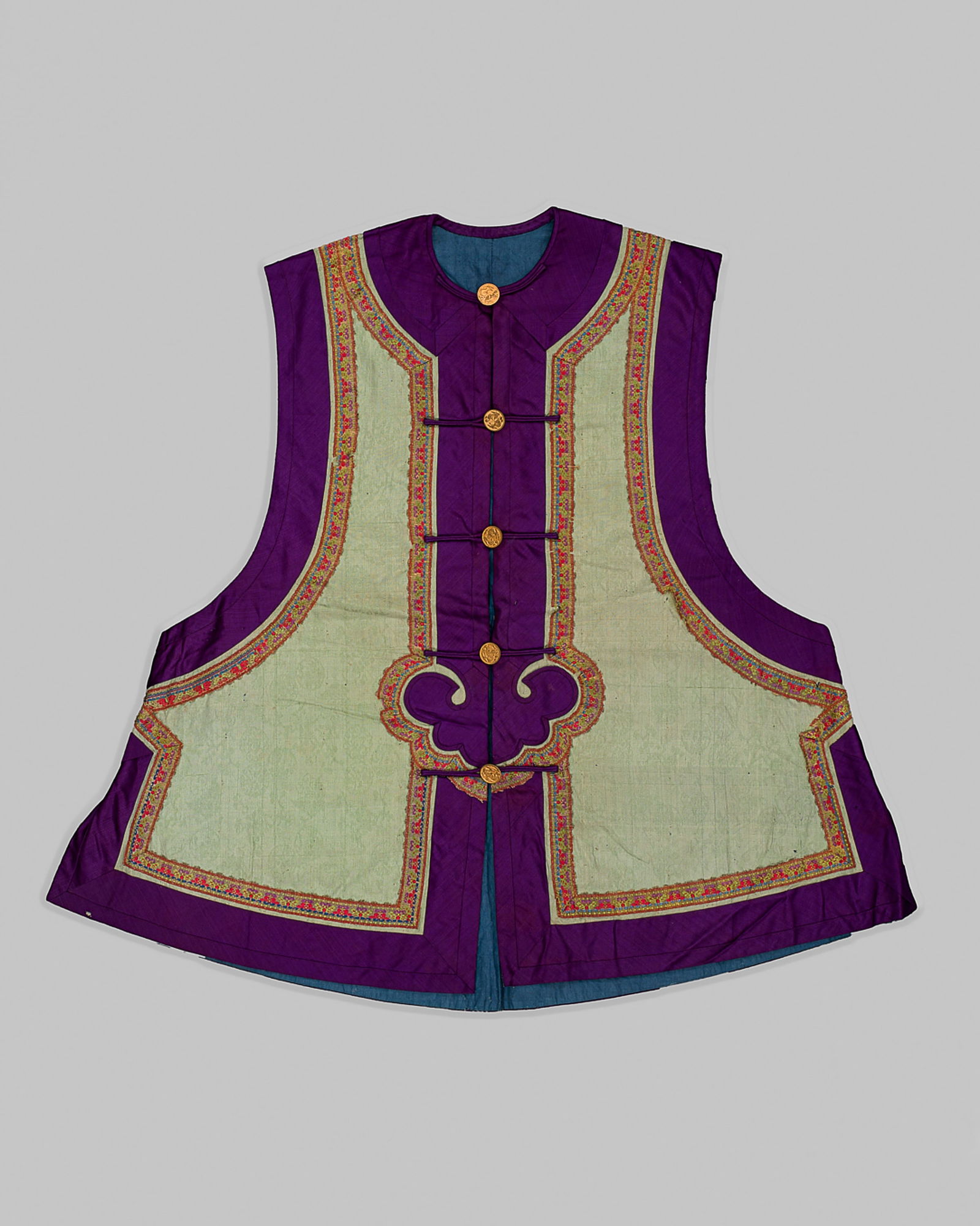 A PURPLE AND TEA-GREEN MANCHU WOMEN'S VEST, LATE QING DYNASTY: A PURPLE AND TEA-GREEN MANCHU WOMEN'S VEST, LATE QING DYNASTY China, c. 1900s. Designed to be worn over an informal robe, with a center-front closure with five circular metal buttons, each bearing a p