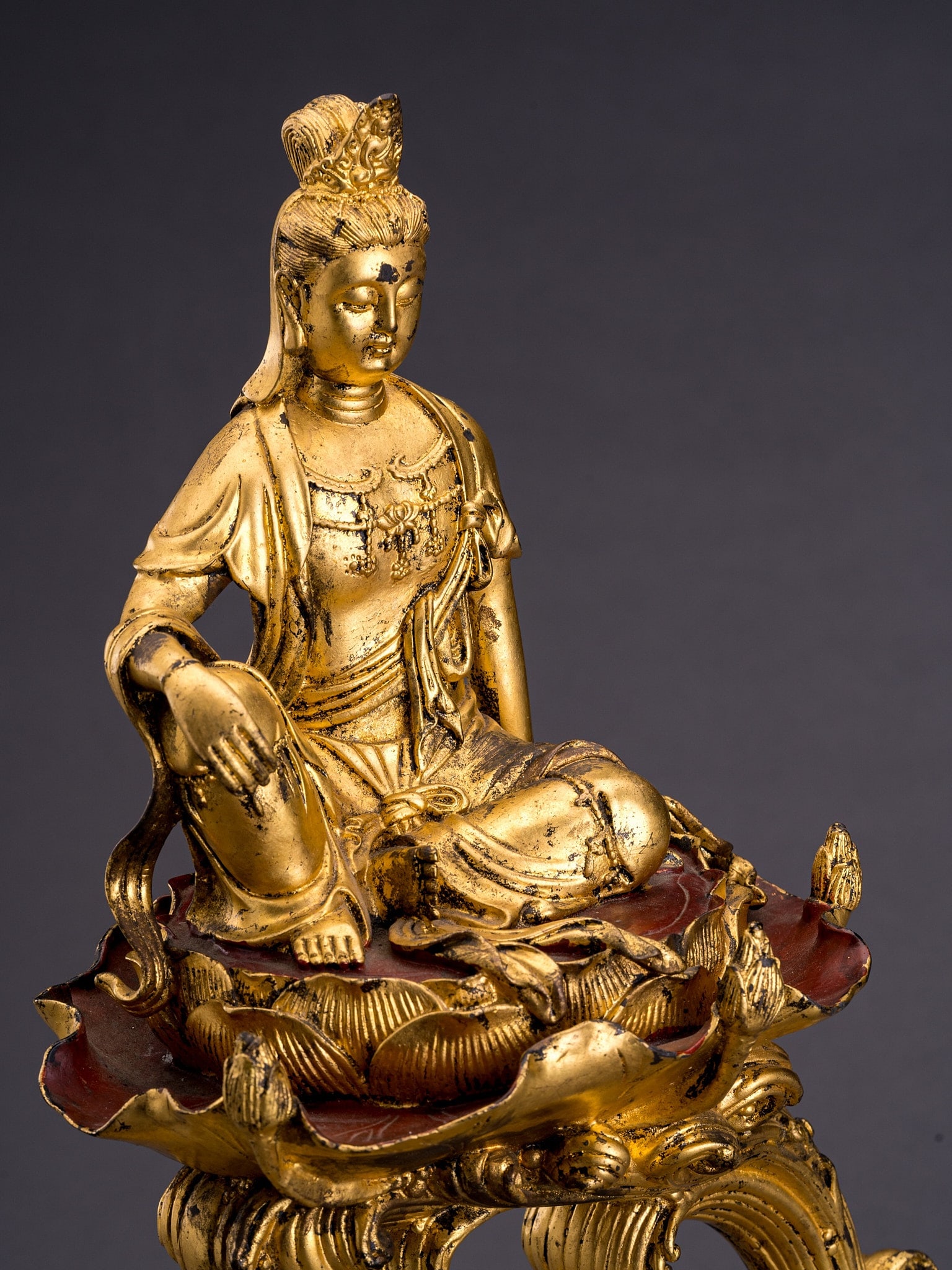 AN UNUSUAL GILT BRONZE FIGURE OF GUANYIN: AN UNUSUAL GILT BRONZE FIGURE OF GUANYIN China, 20th century. Seated in rajalalitasana on a lotus base floating on crashing waves, adorned in beaded jewelry and dressed in a fine robe, the face with d