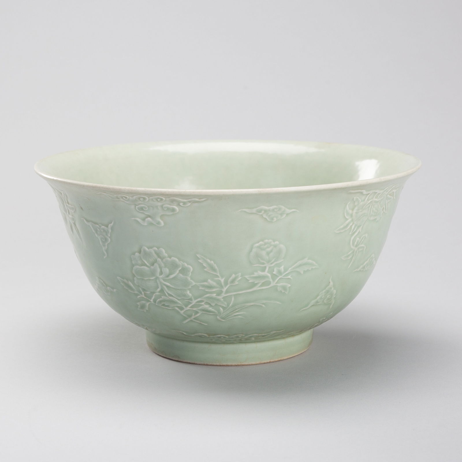 A PALE CELADON 'AUSPICIOUS FLOWERS' PORCELAIN BOWL, 1900s: A PALE CELADON 'AUSPICIOUS FLOWERS' PORCELAIN BOWL, 1900s China, late Qing dynasty (1644-1912) to Republic period (1912-1949). The bowl with deep walls, finely decorated in relief to the exterior with