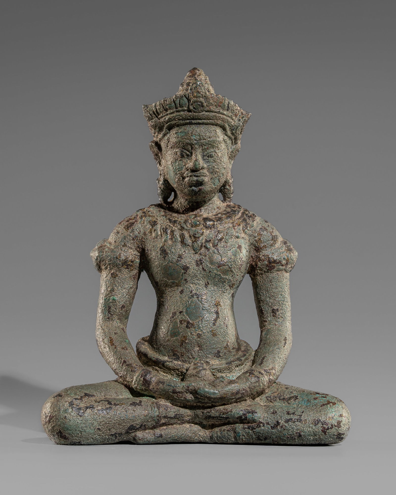 A BRONZE FIGURE OF A CROWNED BUDDHA, ANGKOR PERIOD, 12TH-13TH CENTURY: A BRONZE FIGURE OF A CROWNED BUDDHA, ANGKOR PERIOD, 12TH-13TH CENTURY Khmer Empire. Seated in dhyanasana, with his hands resting on his lap in dhyana mudra, while holding a small alms bowl. The figure