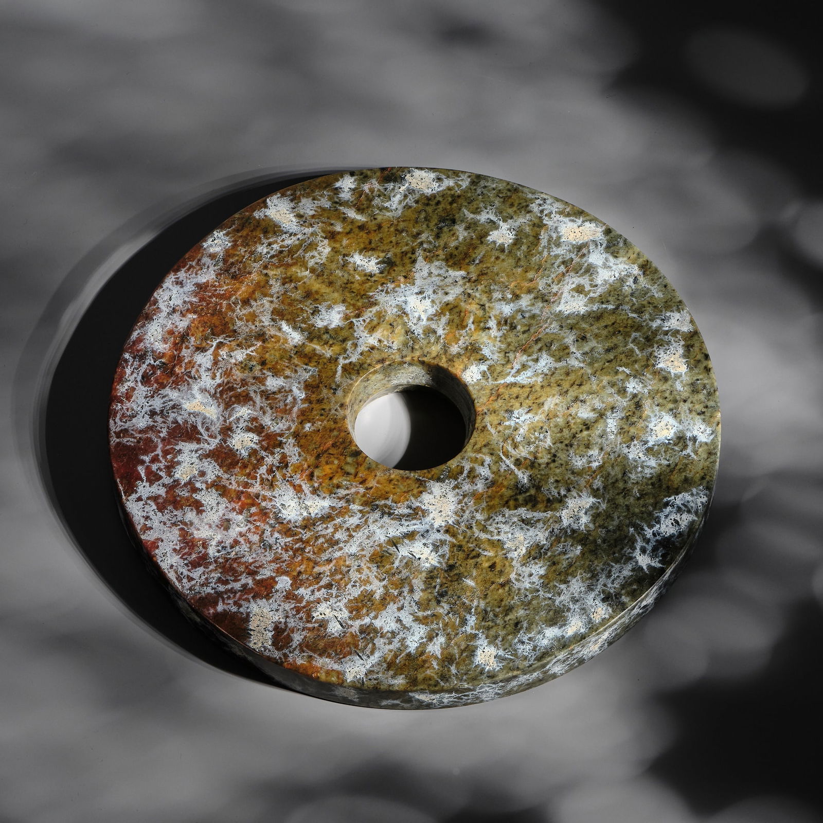 AN EXCEPTIONALLY THICK (1.6 CM) SPINACH GREEN AND RUSSET JADE 'CLOUDED' DISK (BI), LATE NEOLITHIC: AN EXCEPTIONALLY THICK (1.6 CM) SPINACH GREEN AND RUSSET JADE 'CLOUDED' DISK (BI), LATE NEOLITHIC PERIOD, LIANGZHU CULTURE China, c. 3300-2250. Of circular form, with a central aperture drilled from