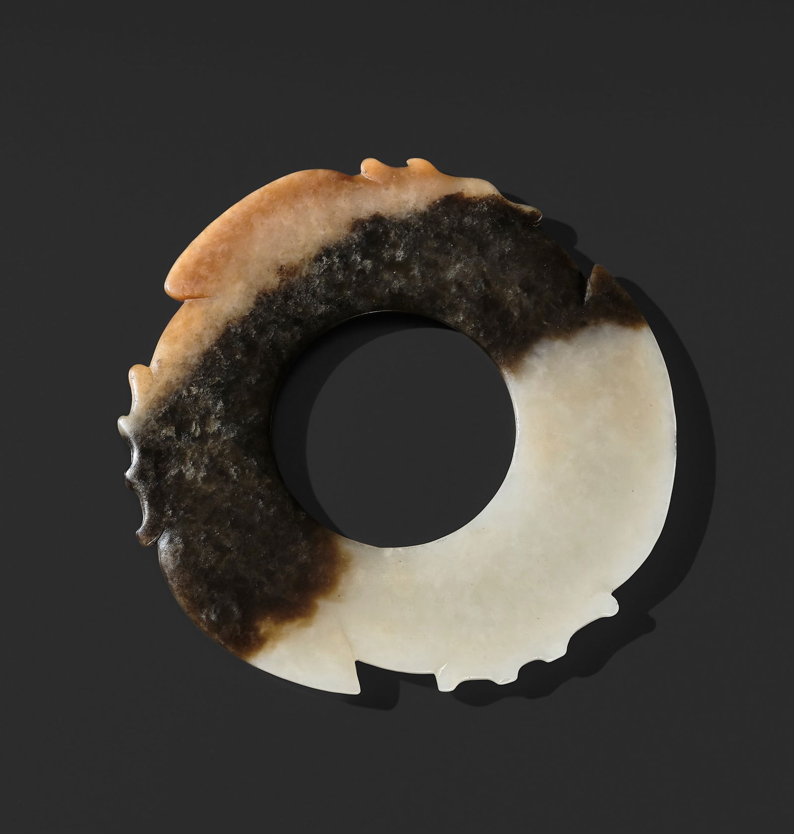 A RARE WHITE, BROWN, AND RUSSET JADE NOTCHED DISK (YABI), LATE NEOLITHIC PERIOD, DAWENKOU OR: A RARE WHITE, BROWN, AND RUSSET JADE NOTCHED DISK (YABI), LATE NEOLITHIC PERIOD, DAWENKOU OR LONGSHAN CULTURE China, c. 2200-2000 BC. Of circular form, the outer rim finely carved with three pronounc