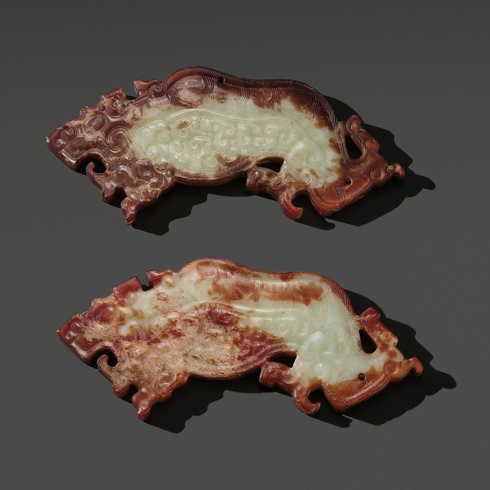 A RARE AND MAGNIFICENT PAIR OF PALE CELADON AND RUSSET JADE 'TIGER' PENDANTS, WARRING STATES PERIOD: A RARE AND MAGNIFICENT PAIR OF PALE CELADON AND RUSSET JADE 'TIGER' PENDANTS, WARRING STATES PERIOD TO WESTERN HAN DYNASTY China, c. 475 BC-9 AD. Each powerfully carved in the form of a crouching bea