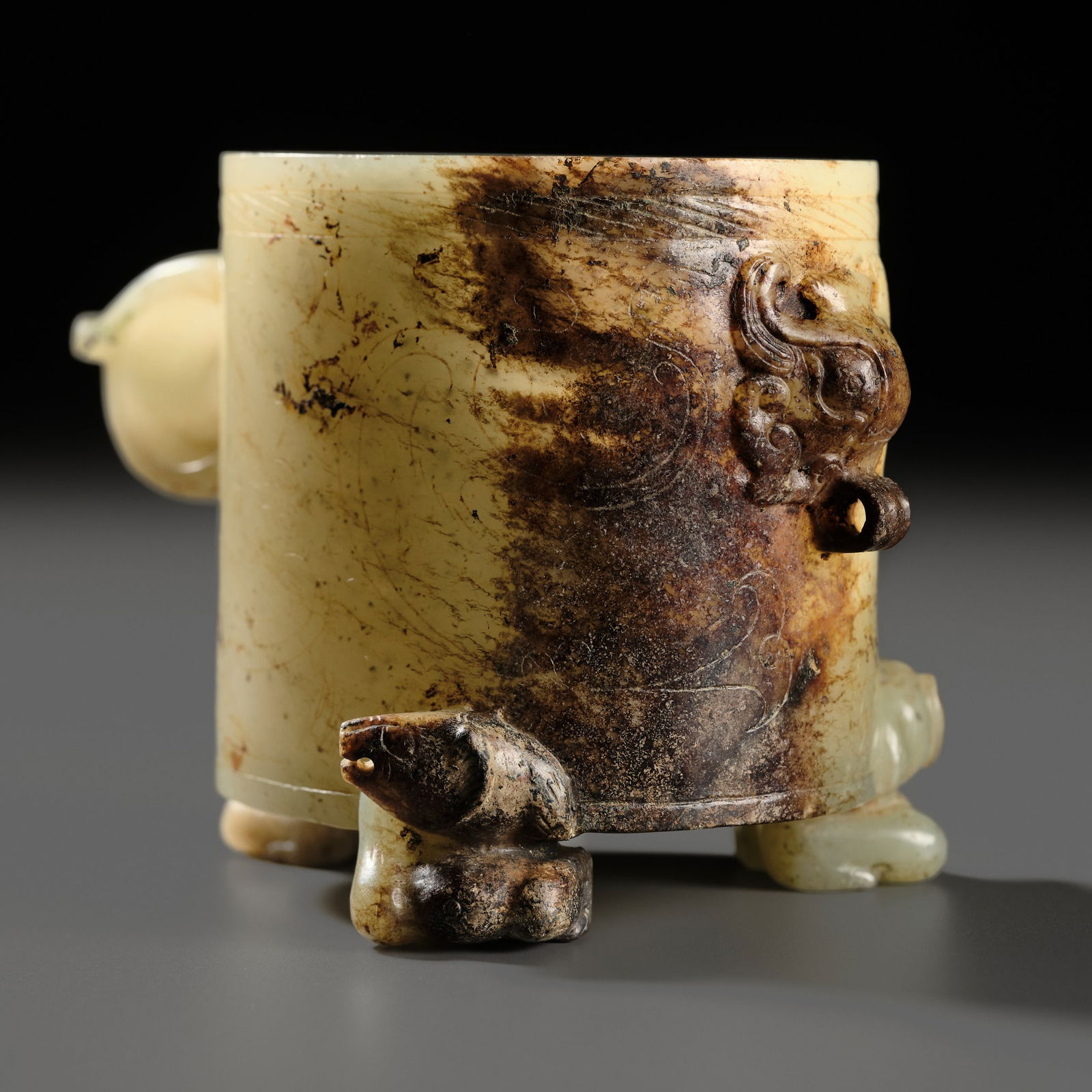A PALE CELADON AND RUSSET JADE WINE CUP, HAN DYNASTY: A PALE CELADON AND RUSSET JADE WINE CUP, HAN DYNASTY China, 206 BC-220 AD. Finely hollowed, of cylindrical form, supported on three small feet shaped as recumbent bears with their heads gently turned