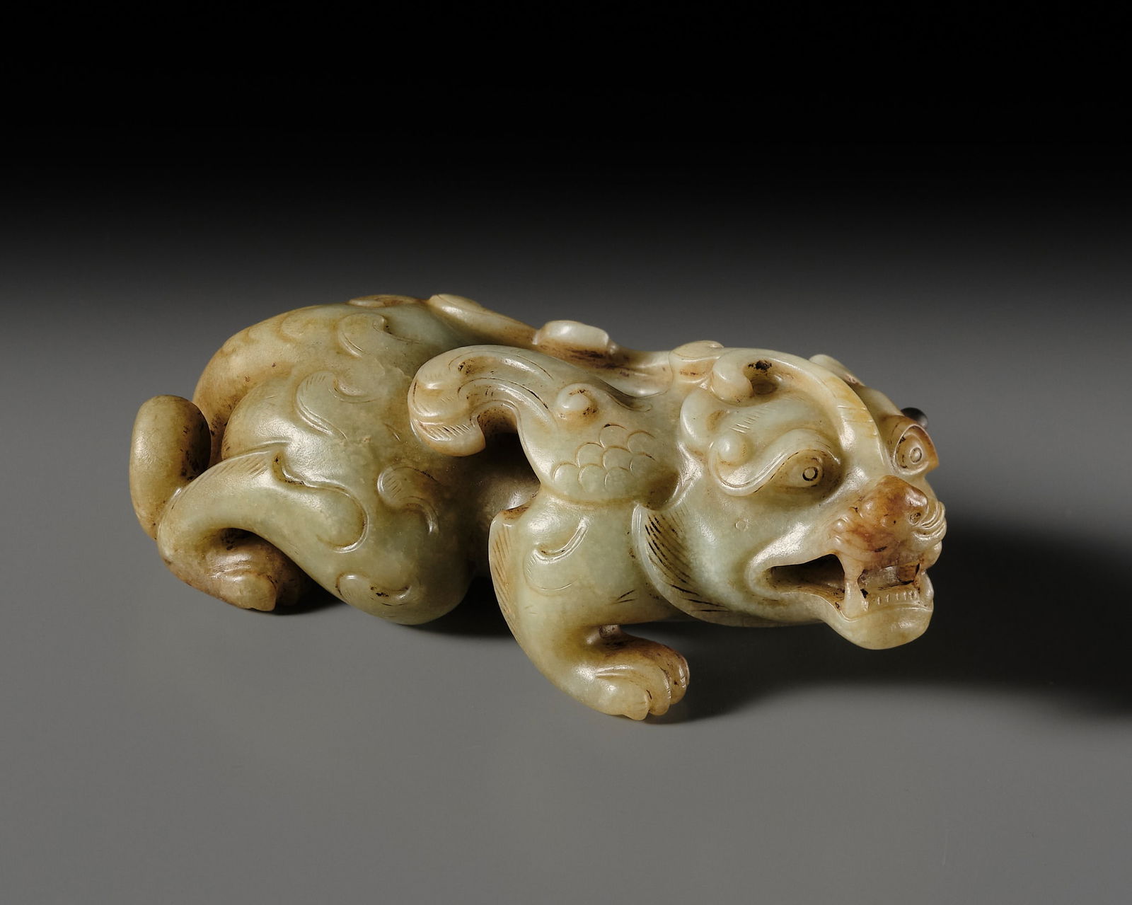 AN ARCHAISTIC JADE FIGURE OF A BIXIE, MING DYNASTY: AN ARCHAISTIC JADE FIGURE OF A BIXIE, MING DYNASTY China, 1368-1644. Carved as a powerful winged beast in a crouching stance, the left front leg extended, the thick paws appearing to firmly grip the