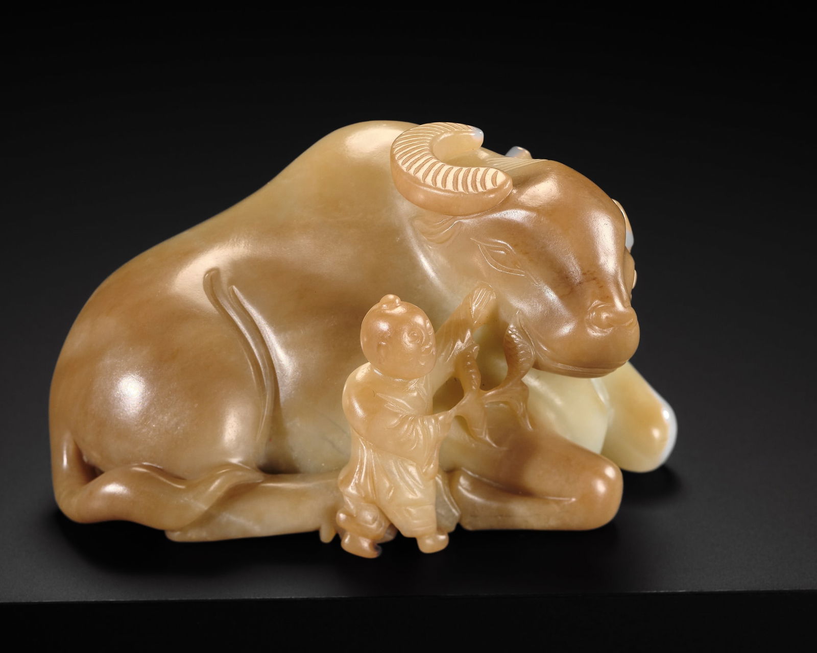 A WHITE AND BROWN JADE 'BUFFALO AND BOY' CARVING, EARLY QING DYNASTY: A WHITE AND BROWN JADE 'BUFFALO AND BOY' CARVING, EARLY QING DYNASTY China, 17th-18th century. Dexterously carved in the round, the majestic water buffalo depicted in a recumbent posture, with legs t