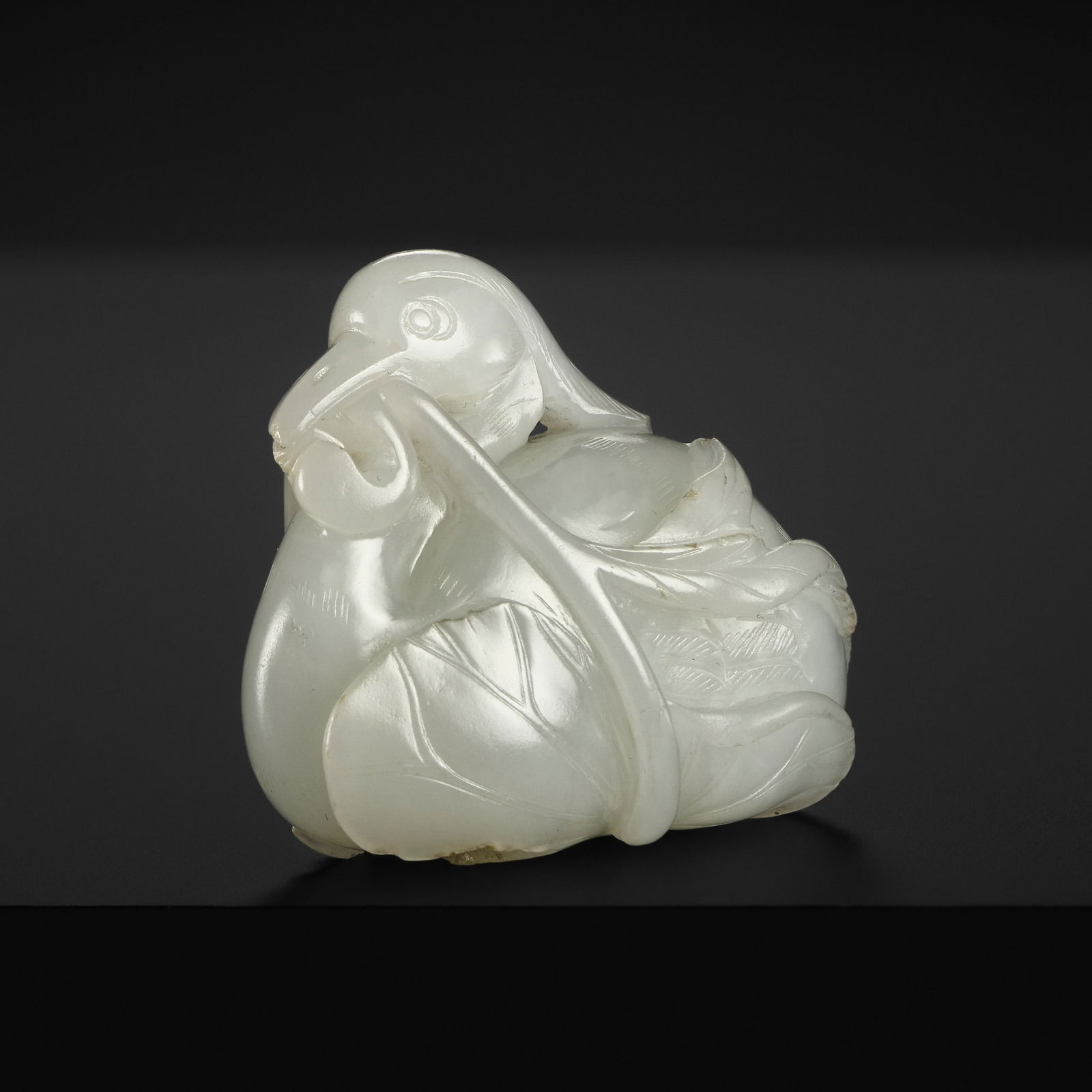 A FINE WHITE JADE 'MANDARIN DUCK AND LOTUS' CARVING, QING DYNASTY: A FINE WHITE JADE 'MANDARIN DUCK AND LOTUS' CARVING, QING DYNASTY China, 18th century. Minutely carved in the form of a reclining duck, its head oriented forward with the sinuous neck drawn closely a