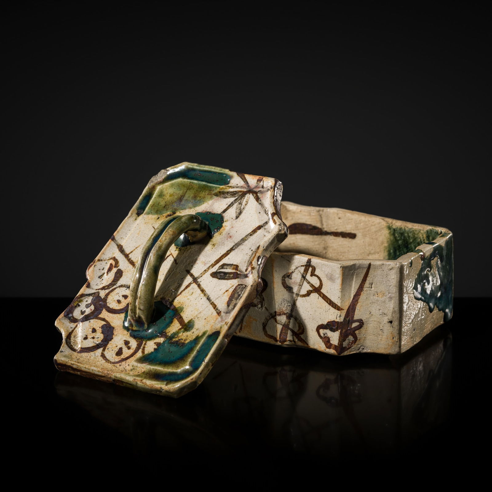AN ORIBE BOX AND COVER, FUTAMONO: AN ORIBE BOX AND COVER, FUTAMONO Japan, 18th-19th century. Of irregular shape, with straight sides, the cover of similar form fitted with a loop handle, and the pale body covered in partly crackled c