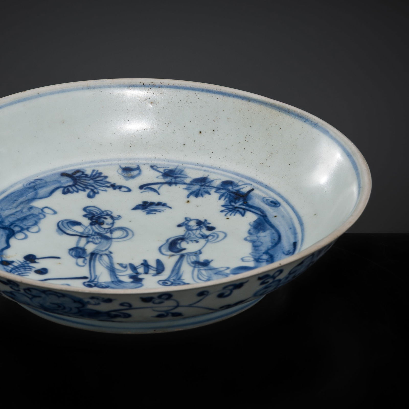 A BLUE AND WHITE 'WINDSWEPT' PORCELAIN SAUCER DISH, MING DYNASTY: A BLUE AND WHITE 'WINDSWEPT' PORCELAIN SAUCER DISH, MING DYNASTY China, possibly Jingdezhen kilns, 15th to 16th century. The deep, rounded sides of the vessel supported on a slightly tapering foot