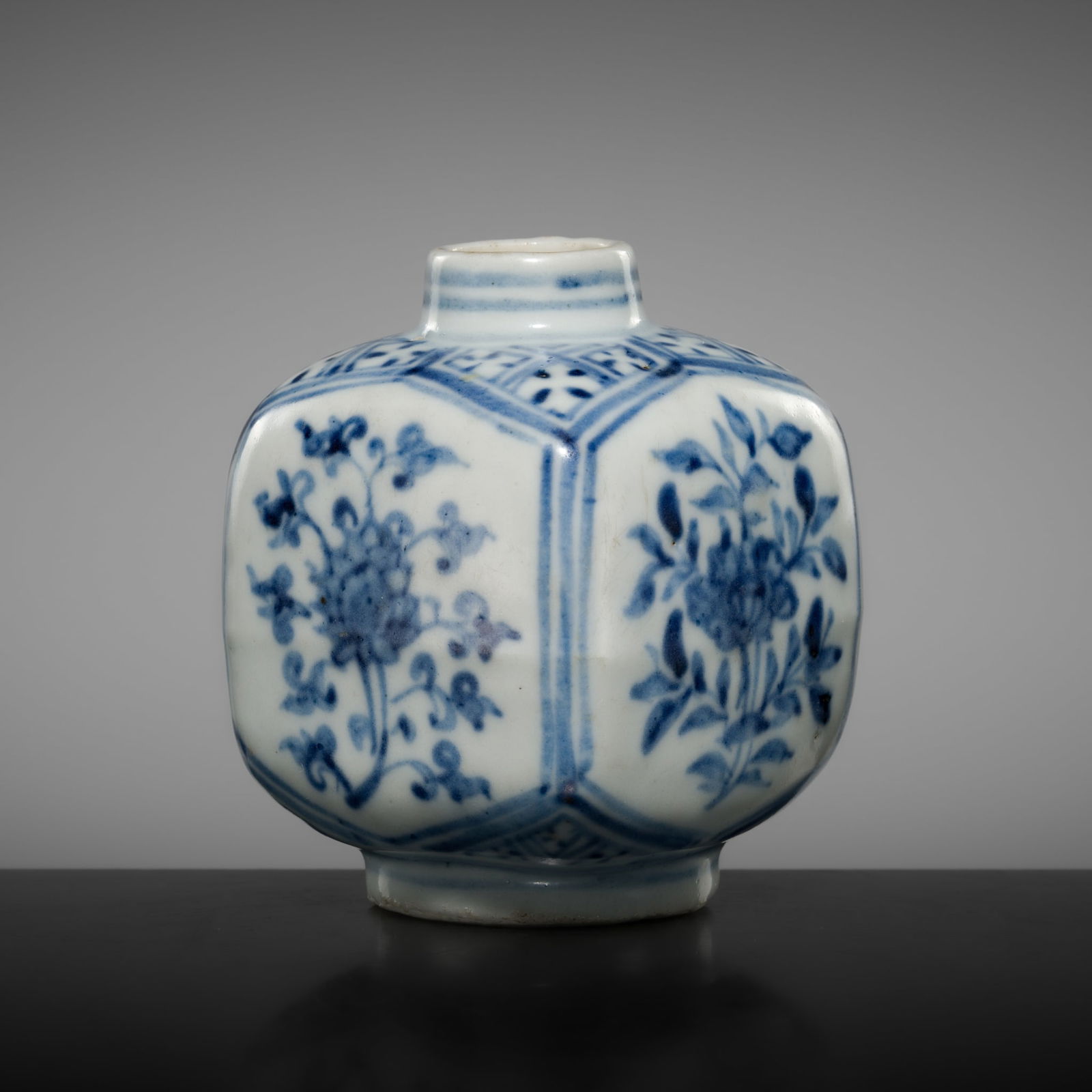 A SMALL BLUE AND WHITE PORCELAIN 'LOTUS AND PEONIES' SQUARED BOTTLE VASE, MING DYNASTY: A SMALL BLUE AND WHITE PORCELAIN 'LOTUS AND PEONIES' SQUARED BOTTLE VASE, MING DYNASTY China, 16th-17th century. Finely potted, the square-section body with softly rounded edges, supported on a short
