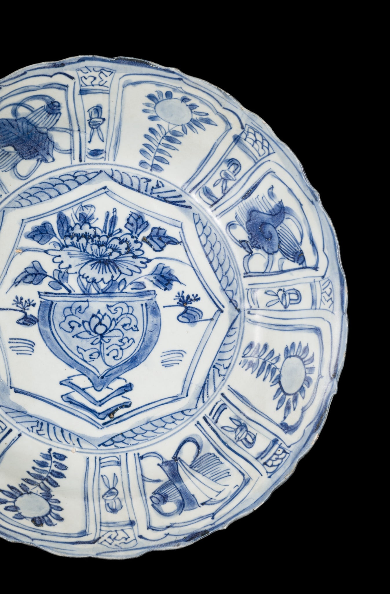 A BLUE AND WHITE 'KRAAK' CHARGER, TRANSITIONAL PERIOD, FROM THE HATCHER CARGO: A BLUE AND WHITE 'KRAAK' CHARGER, TRANSITIONAL PERIOD, FROM THE HATCHER CARGO China, mid-17th century. The central barbed panel painted with an ornate vase holding chrysanthemums, the lobed everted r