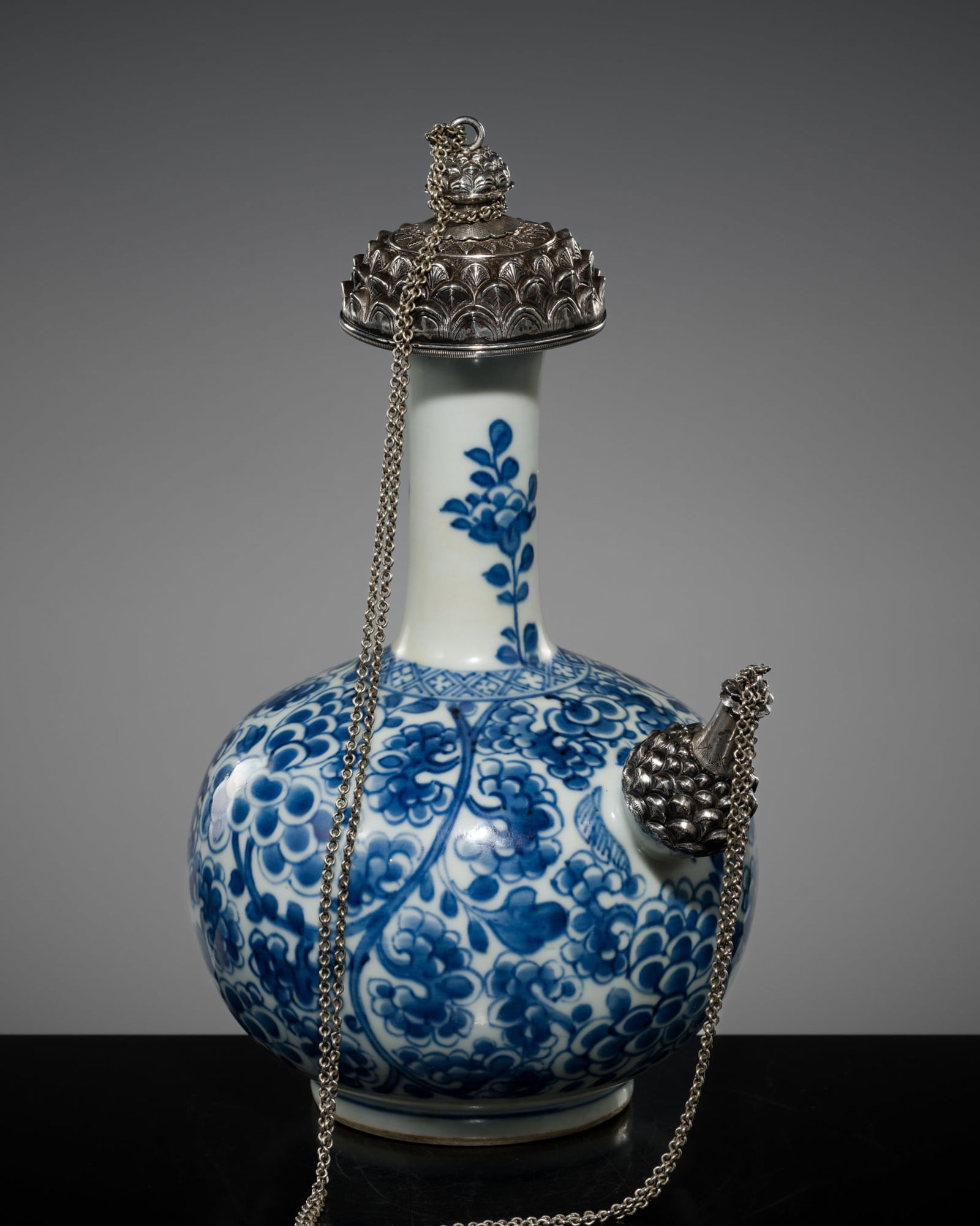 A SILVER-MOUNTED BLUE AND WHITE PORCELAIN 'LOTUS' KENDI, QING DYNASTY, KANGXI PERIOD: A SILVER-MOUNTED BLUE AND WHITE PORCELAIN 'LOTUS' KENDI, QING DYNASTY, KANGXI PERIOD China, 1662-1722. Well potted, the compressed globular body supported on a short, slightly tapered foot and surmou