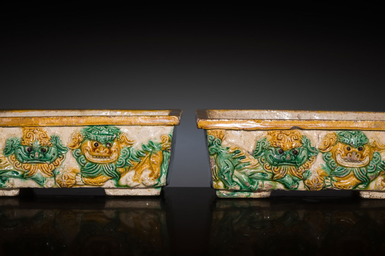 A PAIR OF SANCAI-GLAZED STONEWARE 'BUDDHIST LION' PLANTERS, QING DYNASTY, KANGXI PERIOD: A PAIR OF SANCAI-GLAZED STONEWARE 'BUDDHIST LION' PLANTERS, QING DYNASTY, KANGXI PERIOD China, 1662-1722. Each heavily potted, rectangular in form with tapering sides, supported on four short, L-shap