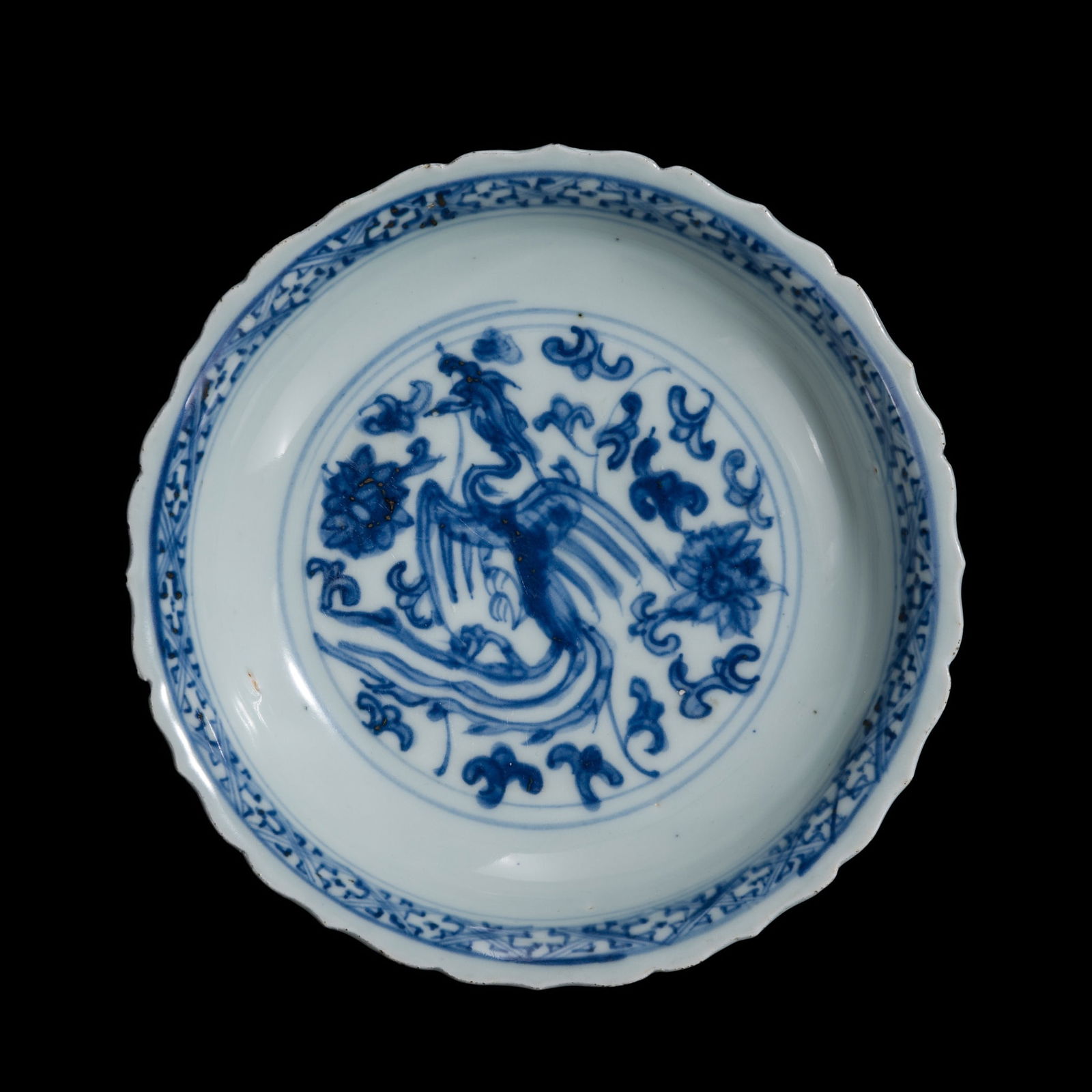 A BARBED BLUE AND WHITE 'PHOENIX' PORCELAIN DISH, QING DYNASTY: A BARBED BLUE AND WHITE 'PHOENIX' PORCELAIN DISH, QING DYNASTY China, 18th-19th century. Finely potted, with deep, rounded sides rising from a short, tapered foot to a slightly everted, lobed rim. Th
