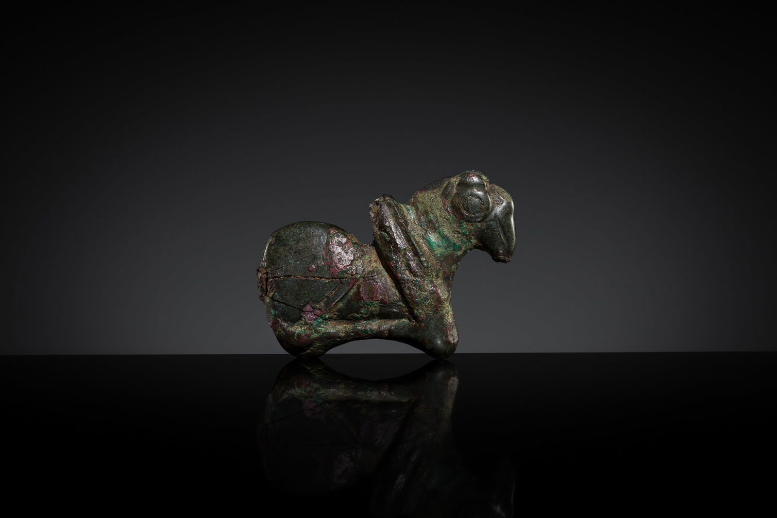 A SMALL AND RARE BRONZE FIGURE OF A RAM, EASTERN ZHOU DYNASTY: A SMALL AND RARE BRONZE FIGURE OF A RAM, EASTERN ZHOU DYNASTY China, c. 770-221 BC. Boldly cast, the recumbent animal is shown in profile, resting with its legs tucked beneath its plump body, which e
