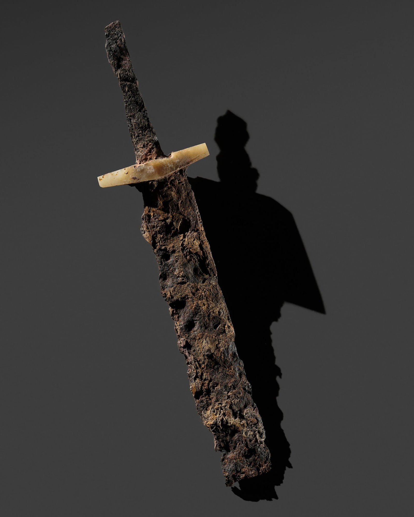 A BRONZE FRAGMENT OF A SWORD WITH A JADE SWORD GUARD, WARRING STATES PERIOD TO HAN DYNASTY: A BRONZE FRAGMENT OF A SWORD WITH A JADE SWORD GUARD, WARRING STATES PERIOD TO HAN DYNASTY China, c. 5th century BC to 2nd century AD. The slender, heavily corroded bronze blade fitted with a rhomboi