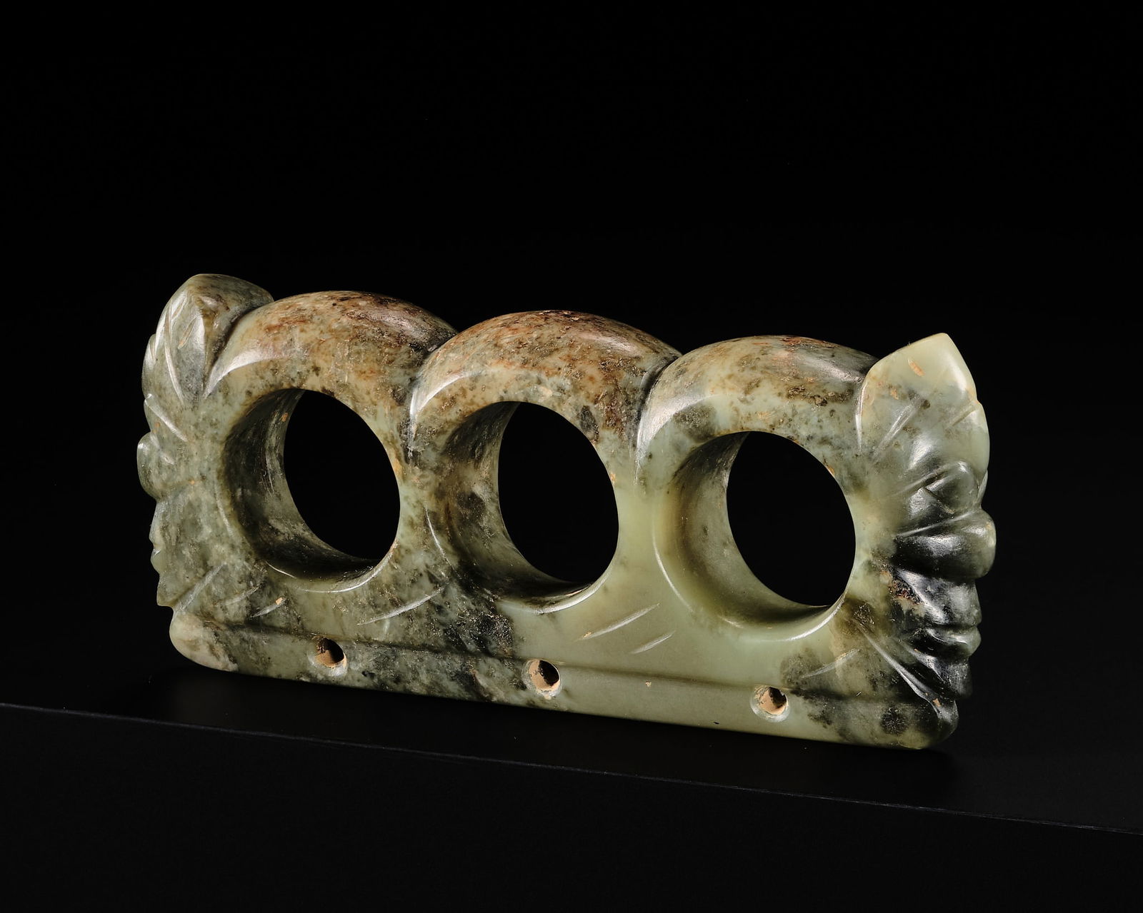 A RARE CELADON JADE TRIPLE RING PENDANT, LATE NEOLITHIC PERIOD, HONGSHAN CULTURE: A RARE CELADON JADE TRIPLE RING PENDANT, LATE NEOLITHIC PERIOD, HONGSHAN CULTURE China, 4700-2500 BC. Of triple-she (thumb ring) form, flanked by human-like heads, each marked by a pair of bulging ey