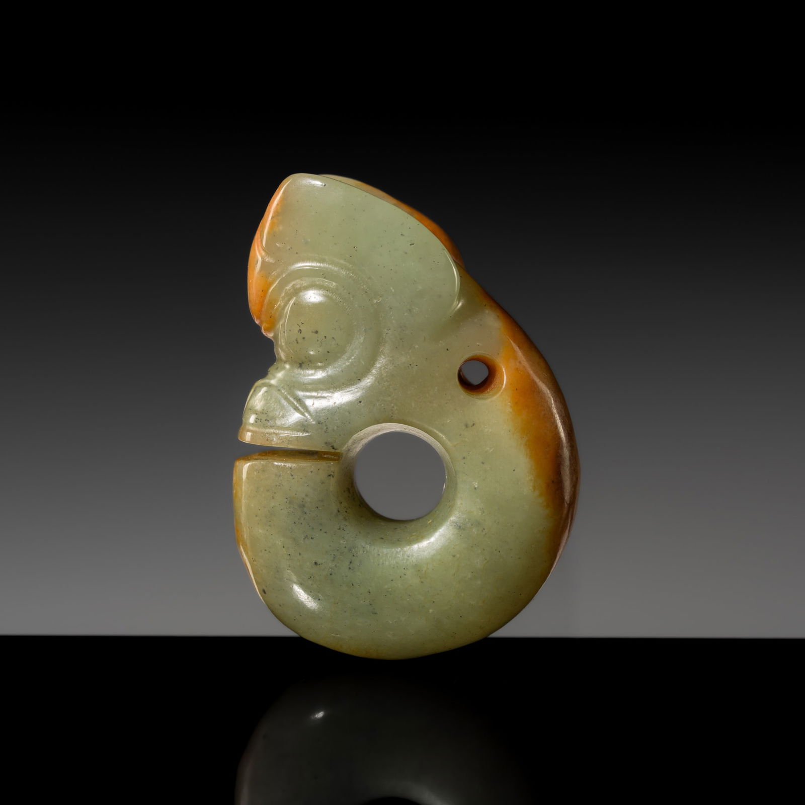 A CELADON AND RUSSET JADE 'PIG-DRAGON' PENDANT, ZHULONG, HONGSHAN CULTURE: A CELADON AND RUSSET JADE 'PIG-DRAGON' PENDANT, ZHULONG, HONGSHAN CULTURE China, Neolithic period, 4700-2500 BC. The coiled body and superbly rendered head subtly detailed with bulging eyes, a wrinkl