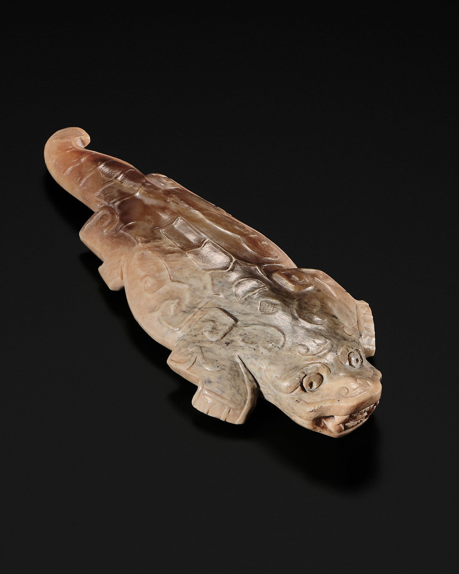 A RARE BROWN JADE 'REPTILE' PENDANT, SHANG DYNASTY: A RARE BROWN JADE 'REPTILE' PENDANT, SHANG DYNASTY China, c. 1600-1050 BC. Of flattened form, the reptile simply but realistically carved with four well-defined limbs, a curling tail, and fierce look