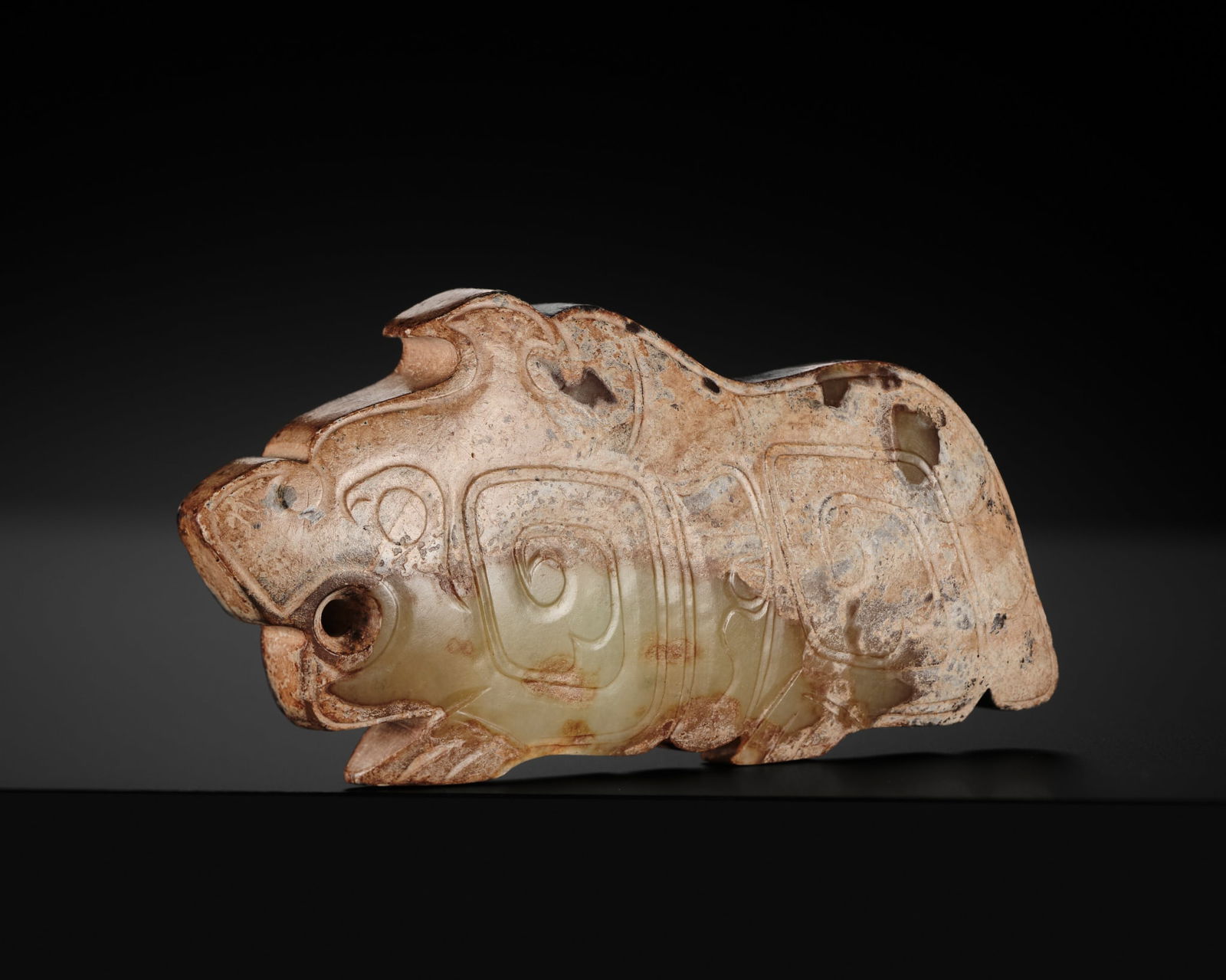 A PALE CELADON JADE 'TIGER' PENDANT, LATE SHANG TO EARLY WESTERN ZHOU DYNASTY: A PALE CELADON JADE 'TIGER' PENDANT, LATE SHANG TO EARLY WESTERN ZHOU DYNASTY China, 12th-10th century BC. The crouching animal finely carved in profile, with its legs tucked beneath the body, decora