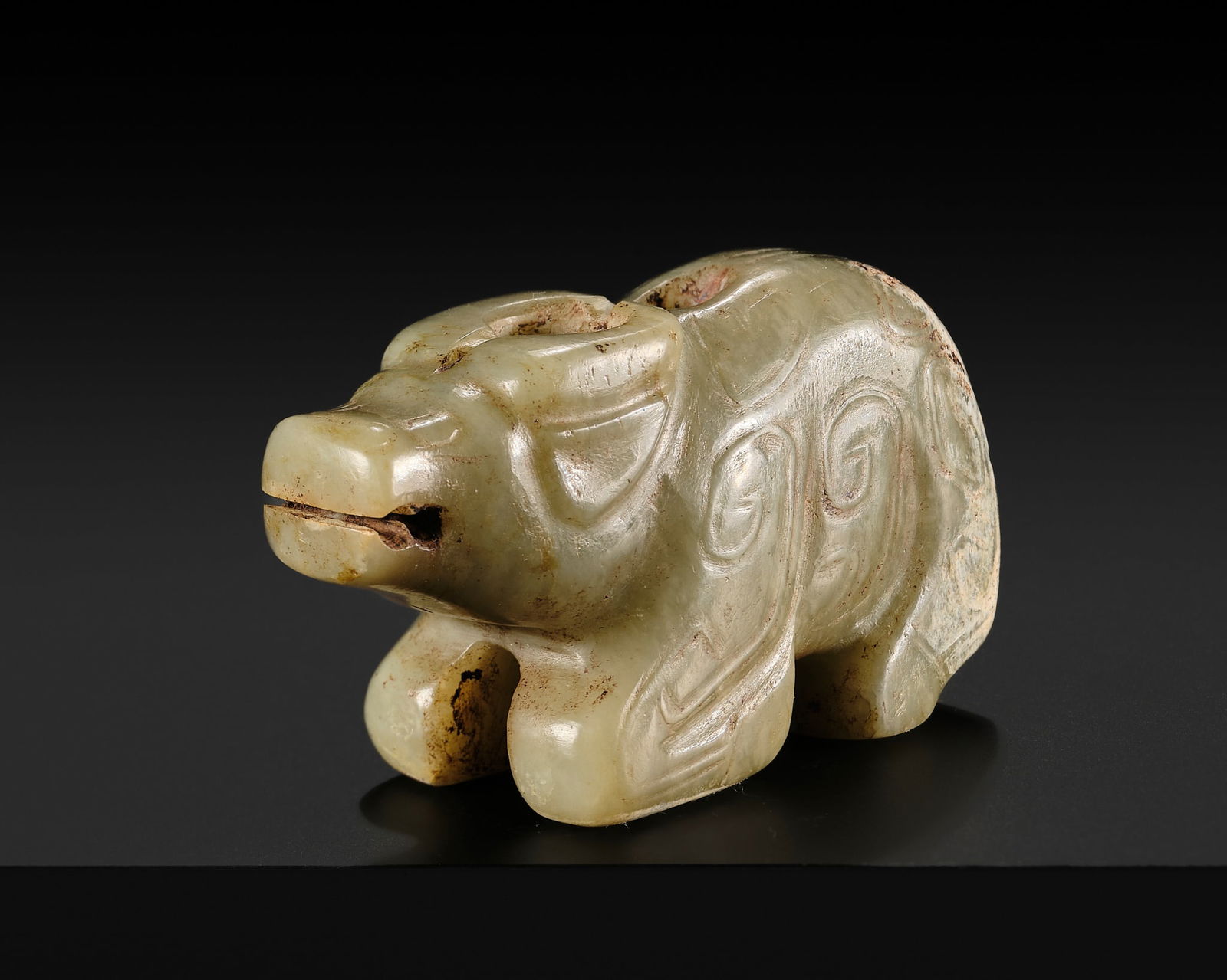 A CELADON JADE 'WATER BUFFALO' PENDANT, LATE SHANG TO EARLY WESTERN ZHOU DYNASTY: A CELADON JADE 'WATER BUFFALO' PENDANT, LATE SHANG TO EARLY WESTERN ZHOU DYNASTY China, c. 13th-11th century BC. Finely carved, the recumbent animal with its legs tucked beneath its plump body, decor